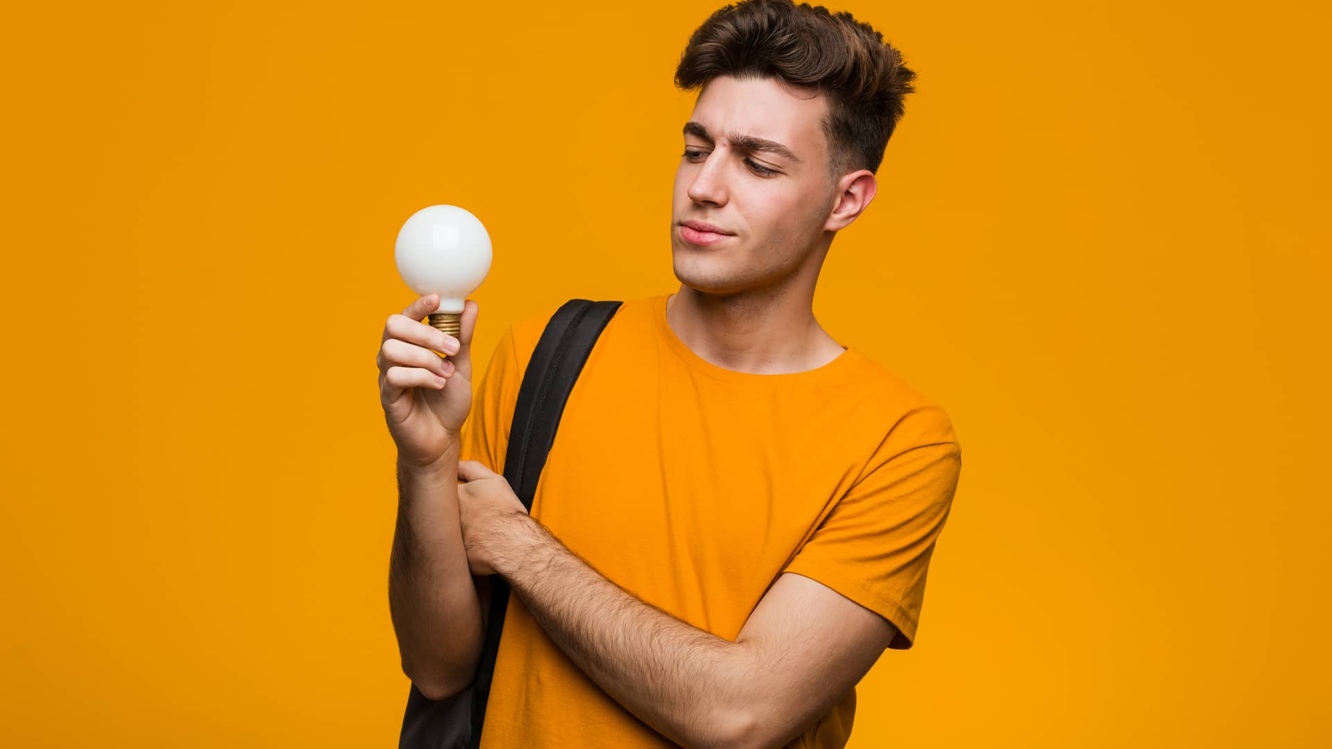Joven mirando una bombilla mientras se pregunta las diferencias entre kw y el kwh Joven mirando una bombilla mientras se pregunta las diferencias entre kw y el kwh
