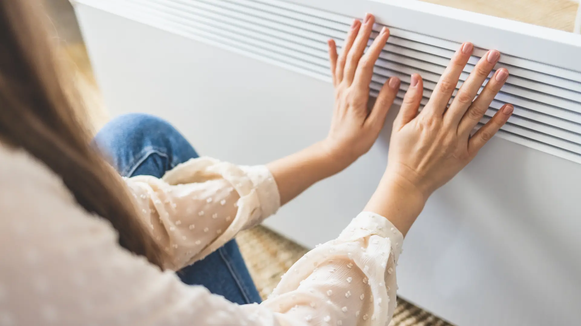Mujer calentandose en un radiador eléctrico, te ayudamos a realizar la elección entre calefacción eléctrica o de gas Mujer calentandose en un radiador eléctrico, te ayudamos a realizar la elección entre calefacción eléctrica o de gas
