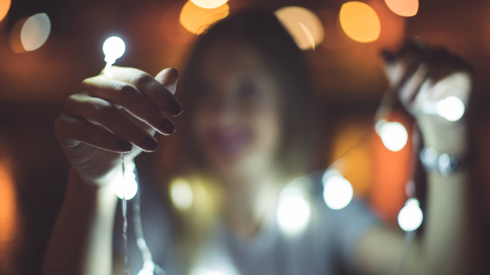 Mujer, que disfruta de una tarifa de luz con precio indexado, coloca una guirnalda de luces de navidad Mujer, que disfruta de una tarifa de luz con precio indexado, coloca una guirnalda de luces de navidad