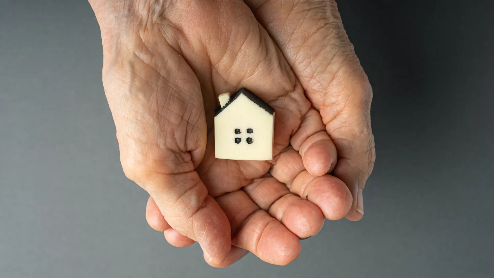 Manos de una persona anciana sujetando una miniatura de una casa para representar la herencia de una vivienda