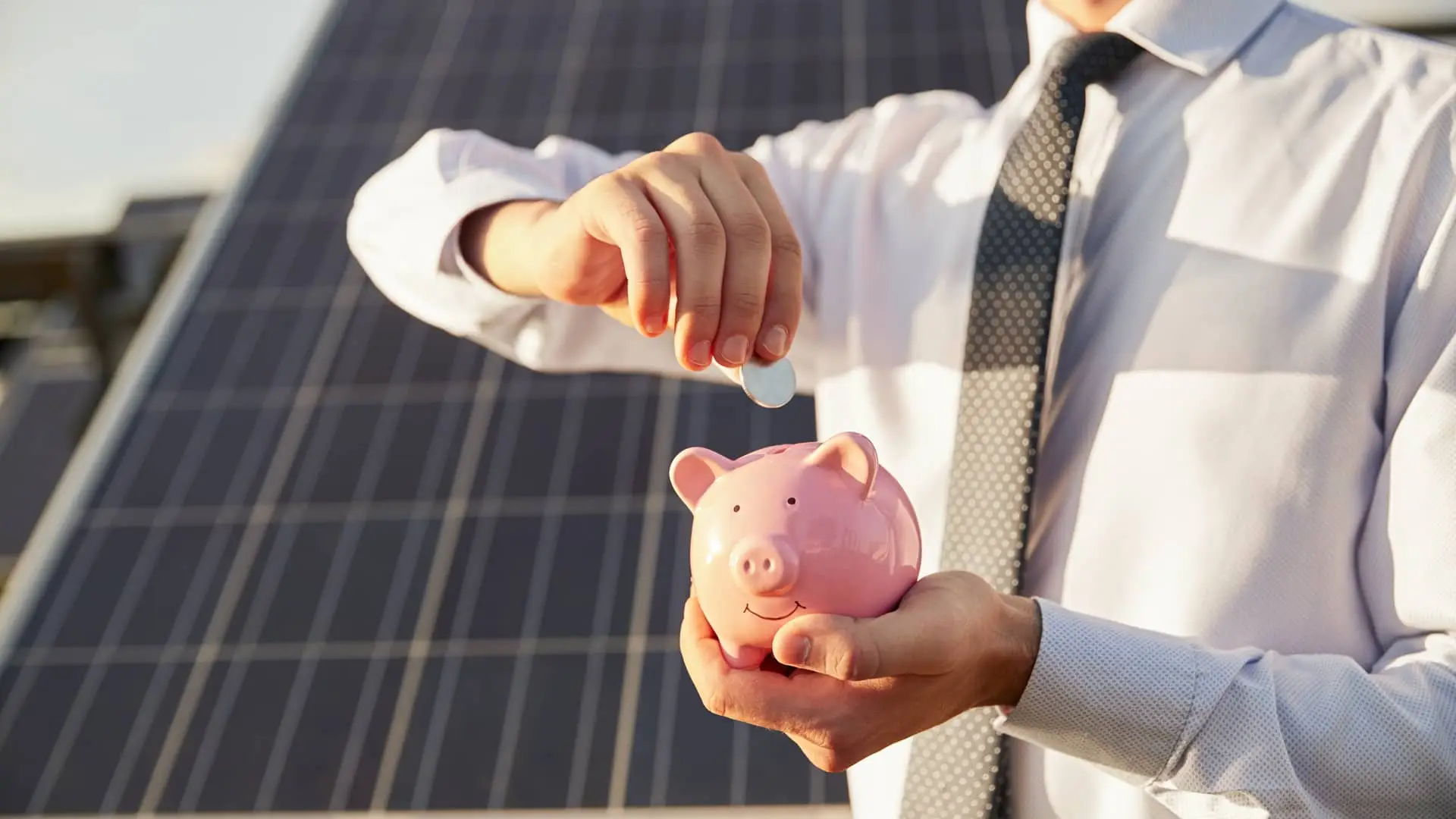 hombre metiendo monedas en un cerdito a modo de inversion delante de unas plazas solares que son energias renovables hombre metiendo monedas en un cerdito a modo de inversion delante de unas plazas solares que son energias renovables