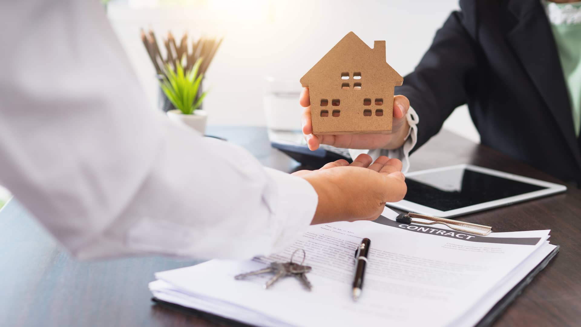Persona entregando una minicasita junto con el contrato de hipoteca representa la doble garantía de poner su otra vivienda como aval