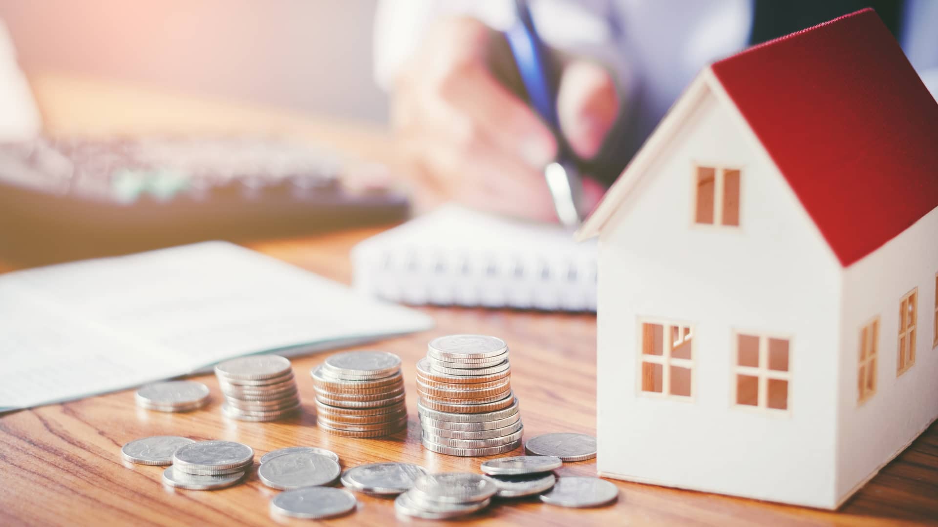 Persona haciendo cuentas junto a una casita de juguete y dinero símboliza el estudio previo que realiza el banco antes de conceder la hipoteca