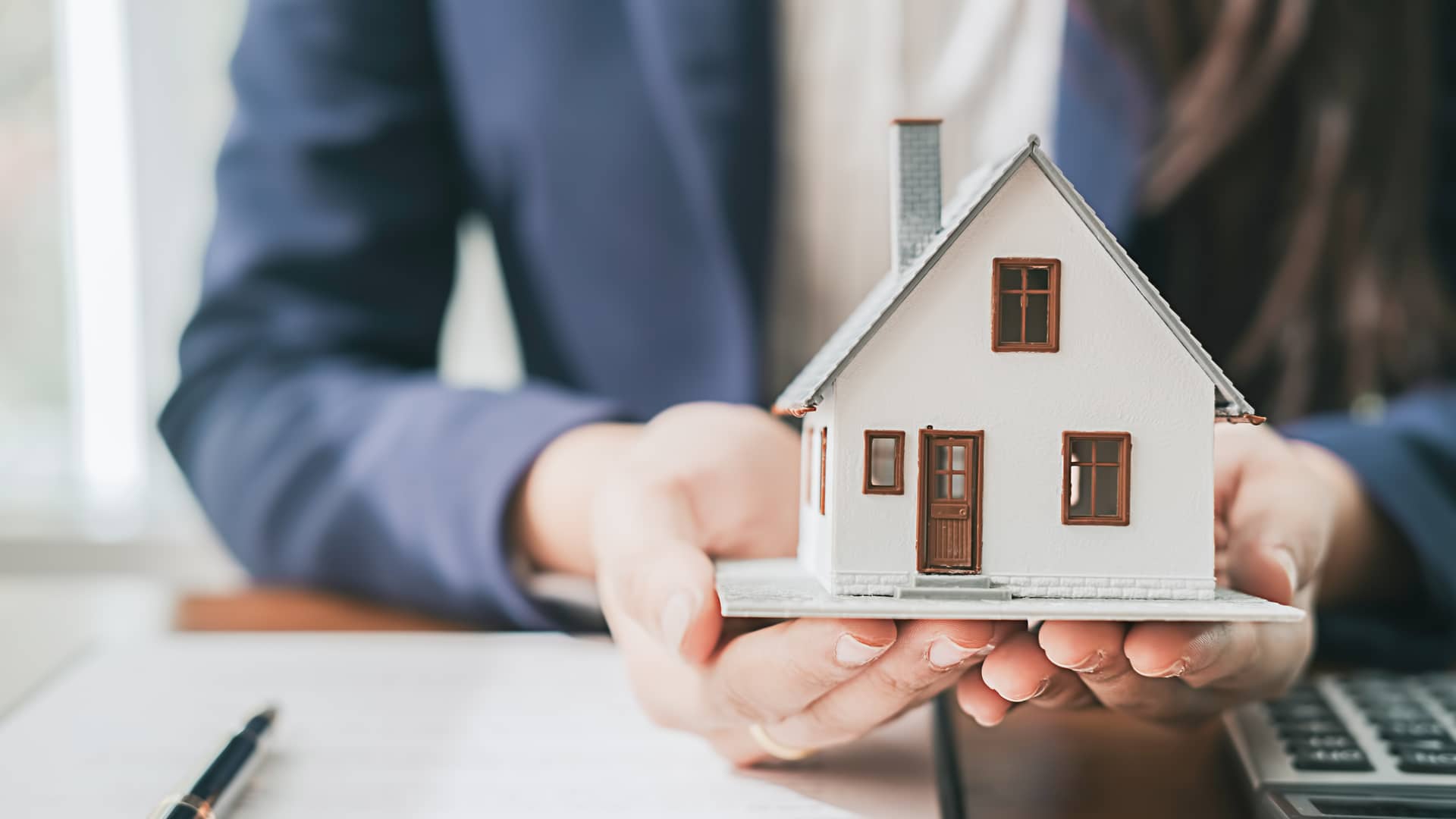 Hombre sosteniendo una maqueta de una casa junto a un contrato símboliza la hipóteca titulizada Hombre sosteniendo una maqueta de una casa junto a un contrato símboliza la hipóteca titulizada