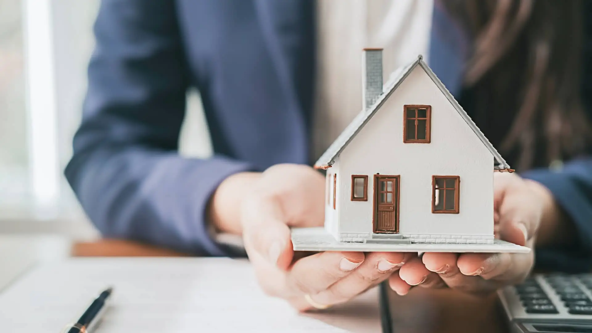 Hombre sosteniendo una maqueta de una casa junto a un contrato símboliza la hipóteca titulizada Hombre sosteniendo una maqueta de una casa junto a un contrato símboliza la hipóteca titulizada