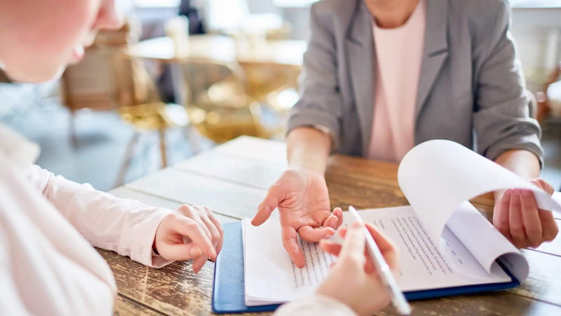 Mujer le explica un contrato a otra mujer representando la novación de su hipóteca Mujer le explica un contrato a otra mujer representando la novación de su hipóteca