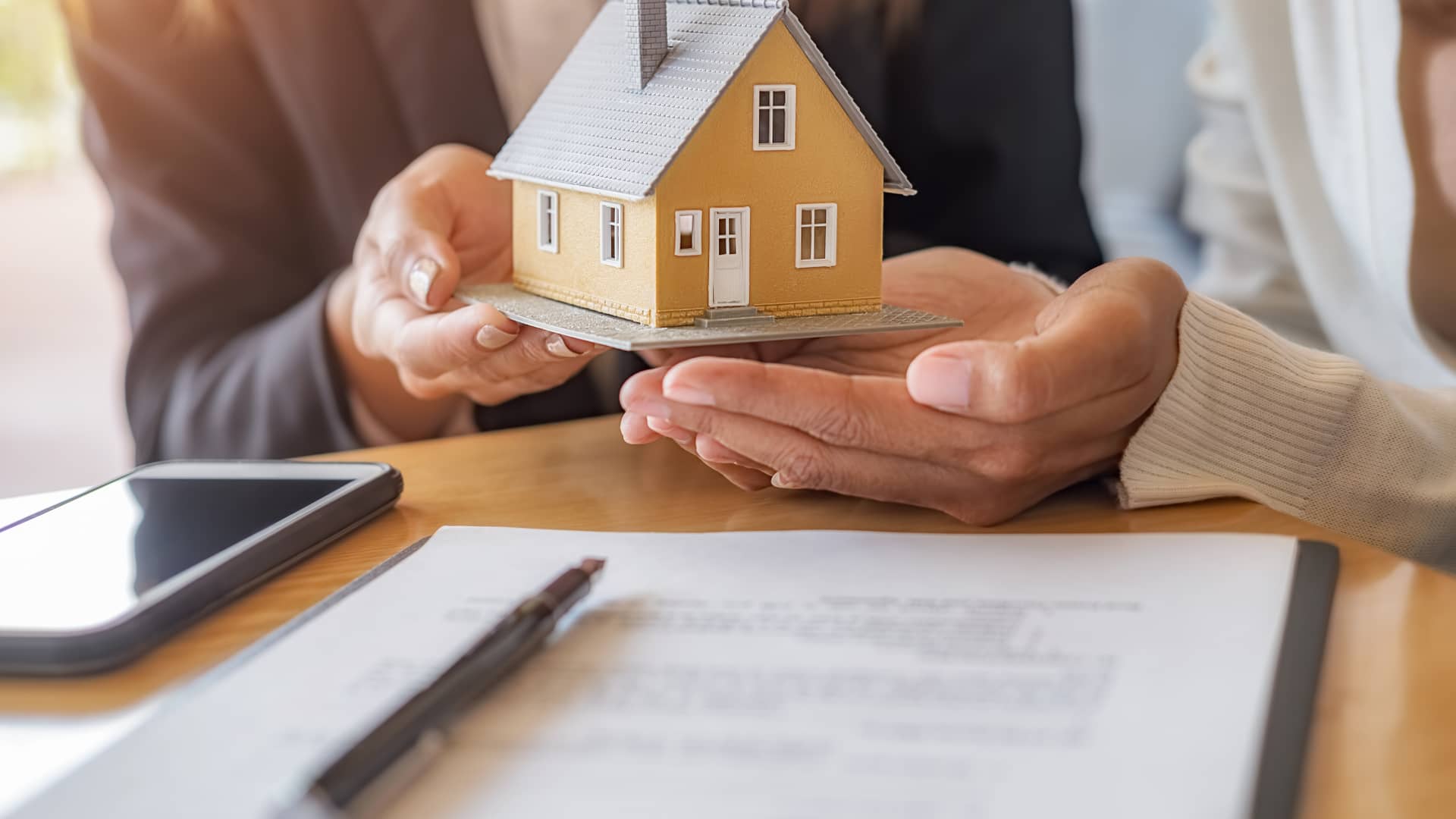 Una persona le entrega a otra una maqueta de una casa, sobre un contrato, representando las hipotecas entre particulares Una persona le entrega a otra una maqueta de una casa, sobre un contrato, representando las hipotecas entre particulares