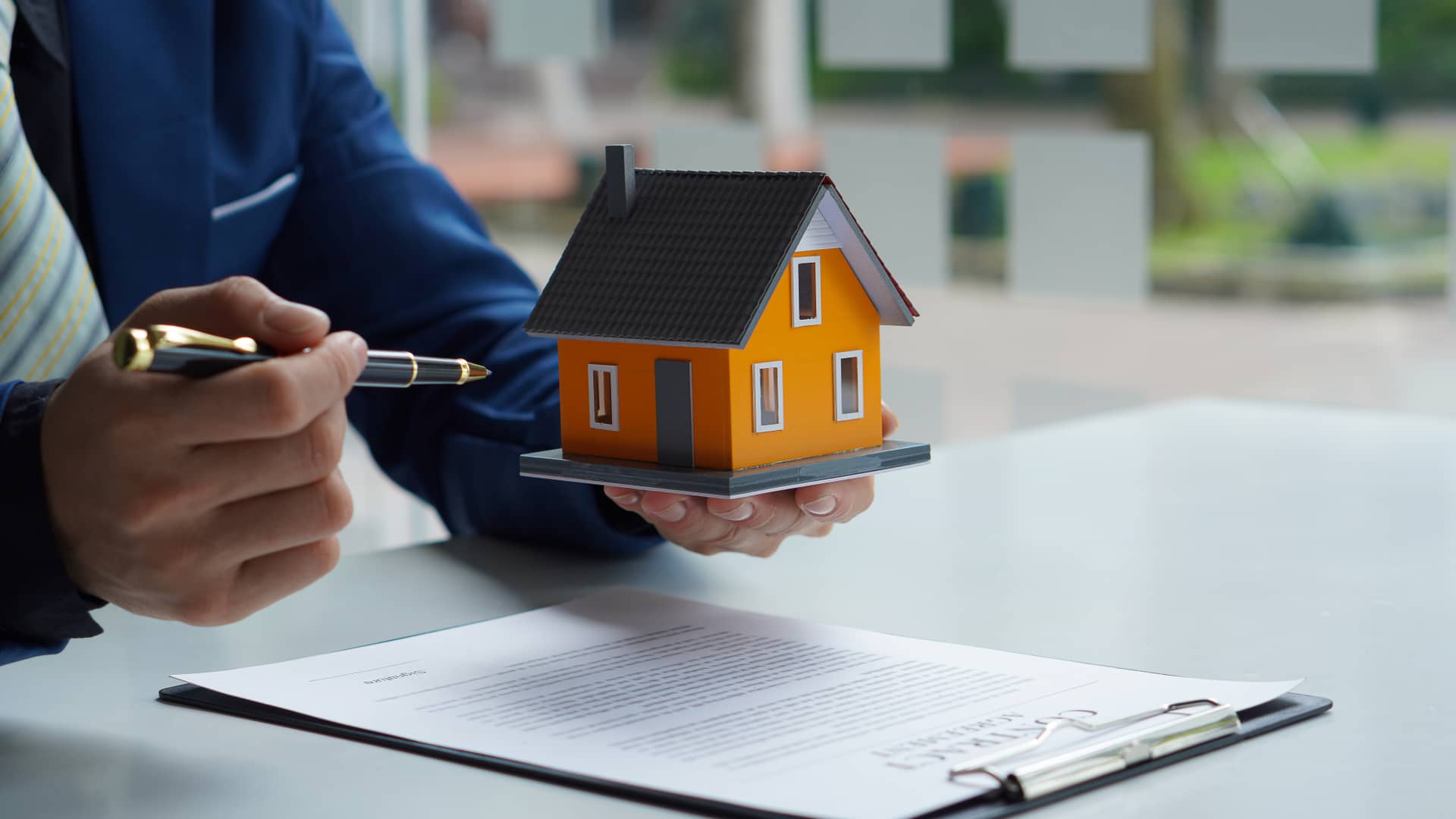 Persona a punto de firmar una hipoteca que ha conseguido pese a no tener contrato fijo, sostiene una maqueta de una casa Persona a punto de firmar una hipoteca que ha conseguido pese a no tener contrato fijo, sostiene una maqueta de una casa