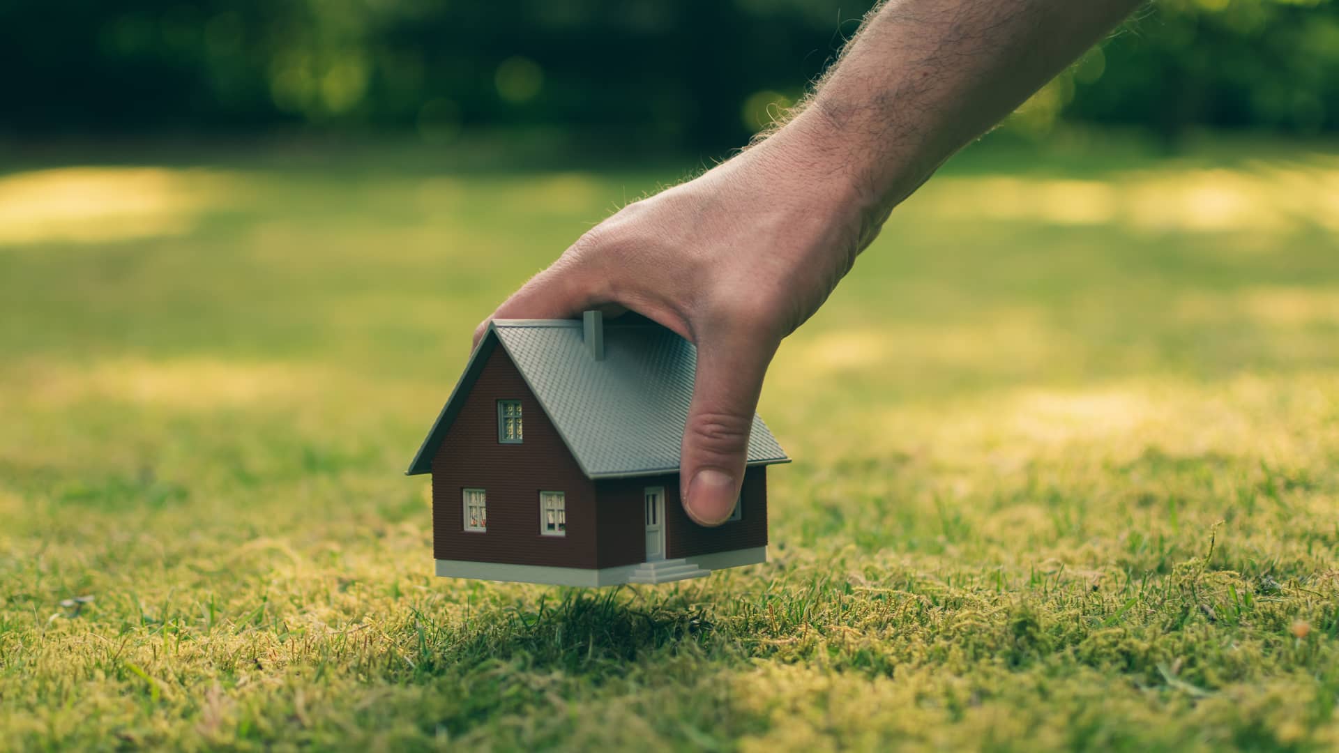 Persona colocando la maqueta de una casa sobre un terreno, representando la posiblidad de solicitar una hipoteca para comprar el terreno sobre el que edificar Persona colocando la maqueta de una casa sobre un terreno, representando la posiblidad de solicitar una hipoteca para comprar el terreno sobre el que edificar