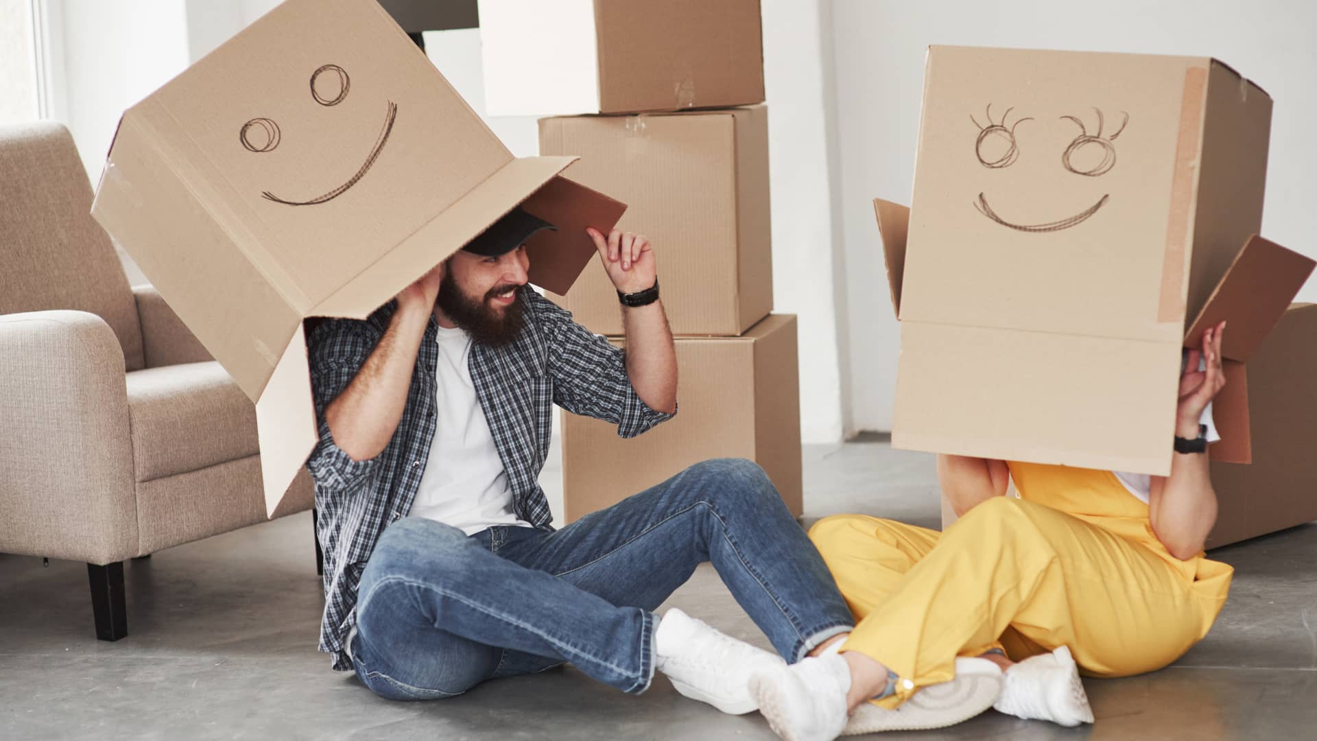 Pareja juega con las cajas de la mudanza con caras de alegría dibujadas, tras conseguir una hipoteca VPO