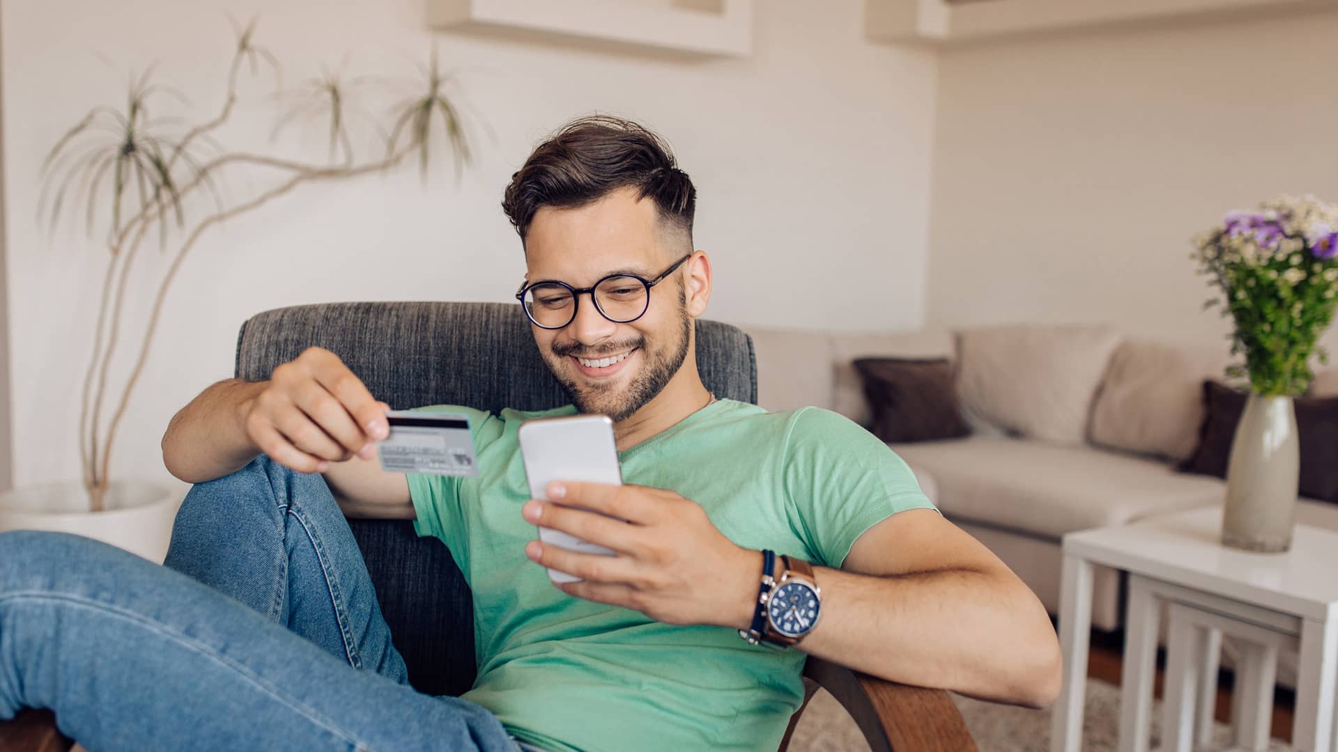 Feliz joven comprando en línea en casa con su tarjeta revolving