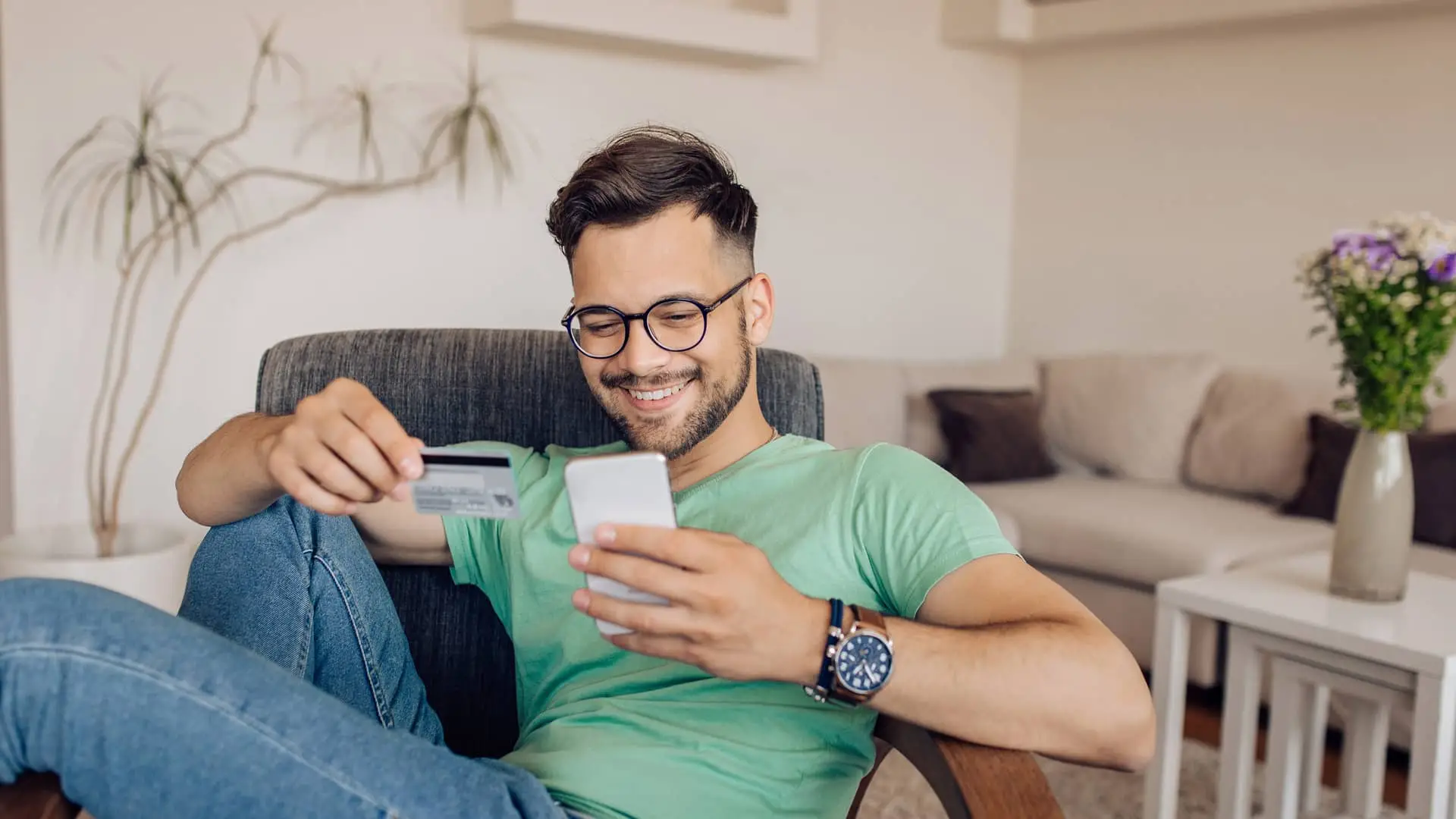 Feliz joven comprando en línea en casa con su tarjeta revolving Feliz joven comprando en línea en casa con su tarjeta revolving