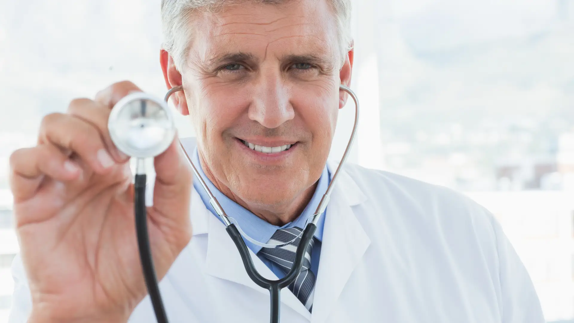 Médico sonriendo a cámara con estetoscopio representando al equipo médico disponible con los seguros de salud adeslas go Médico sonriendo a cámara con estetoscopio representando al equipo médico disponible con los seguros de salud adeslas go