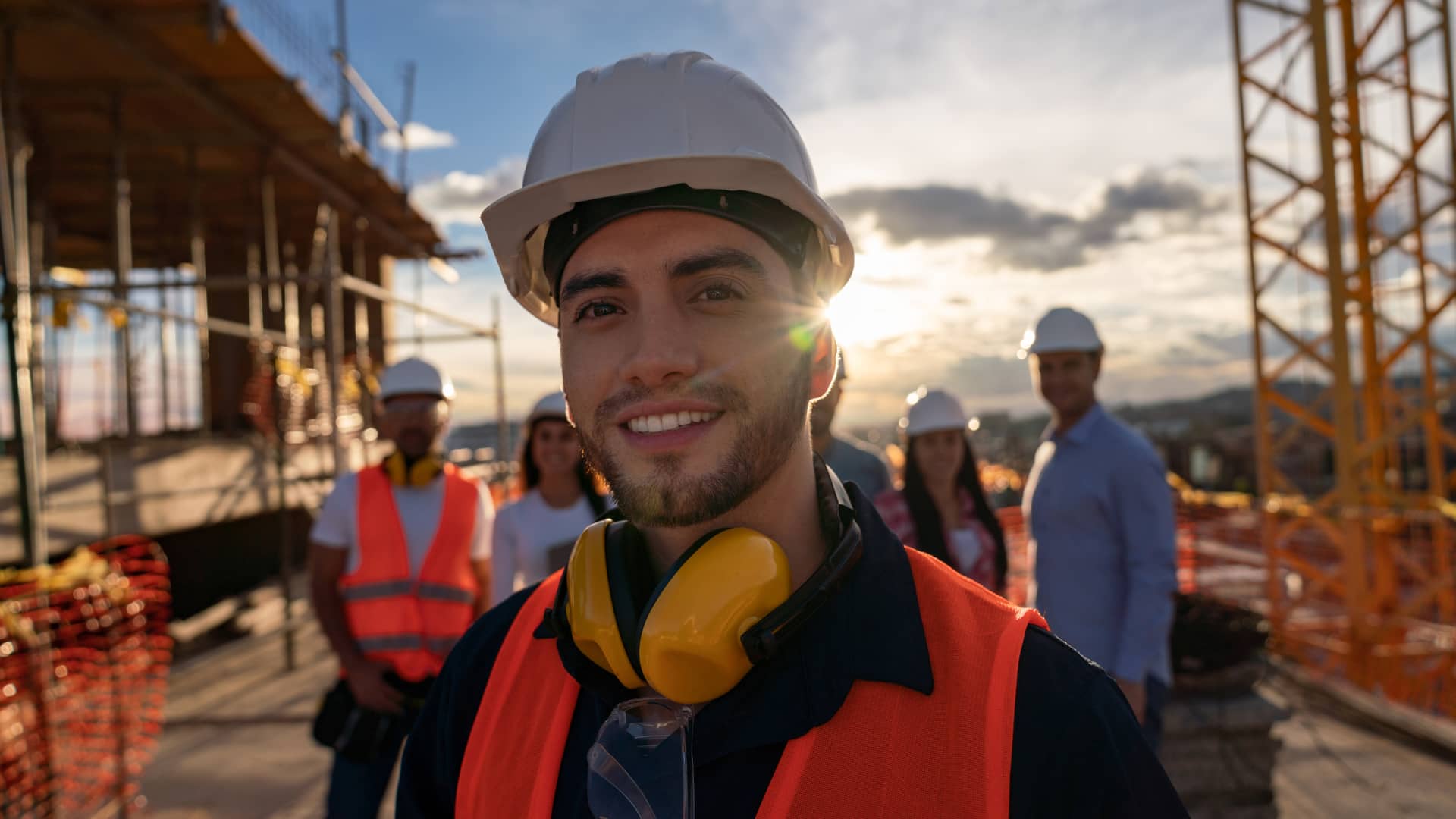 Trabajador de la construcción en primer plano con compañeros de trabajo al fondo, todos ellos protegidos por el seguro de salud de su empresa