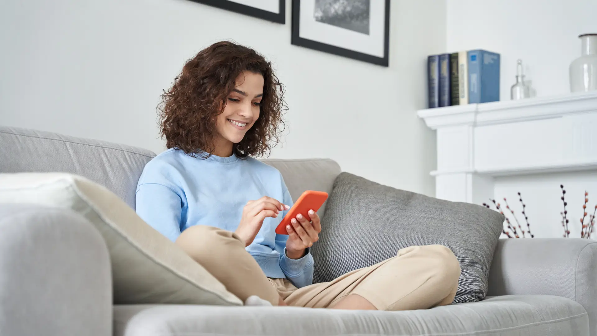 Una chica en el sofa de casa con el movil revisando el area clientes de la aseguradora Allianz