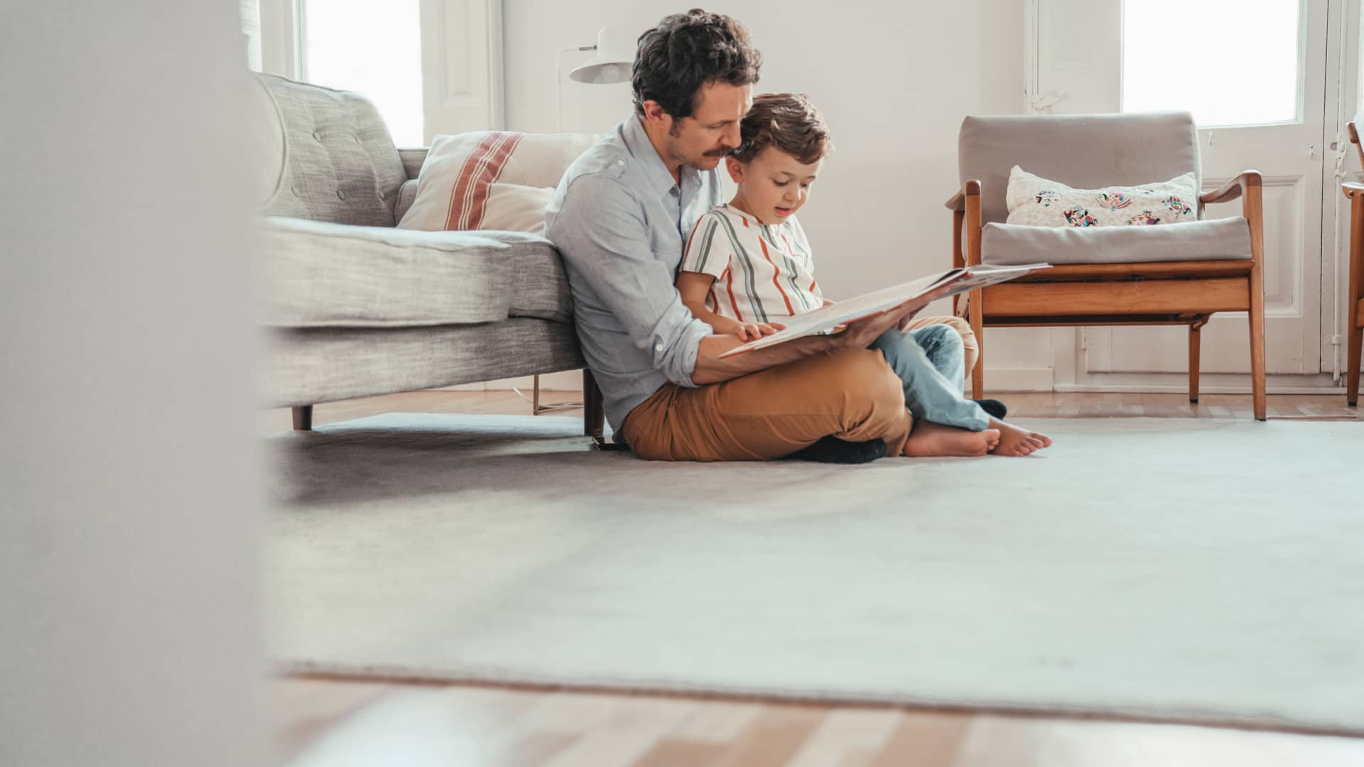 Padre enseñando libro a su hijo sentados en el suelo de su casa con seguro de hogar de allianz