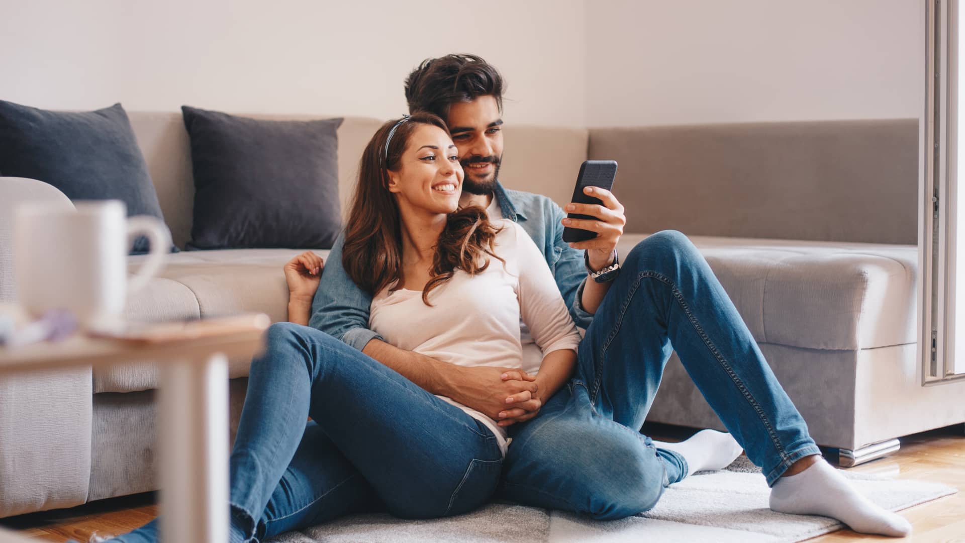 Pareja viendo smartphone tumbados en el suelo de su hogar con seguro de ama contratado