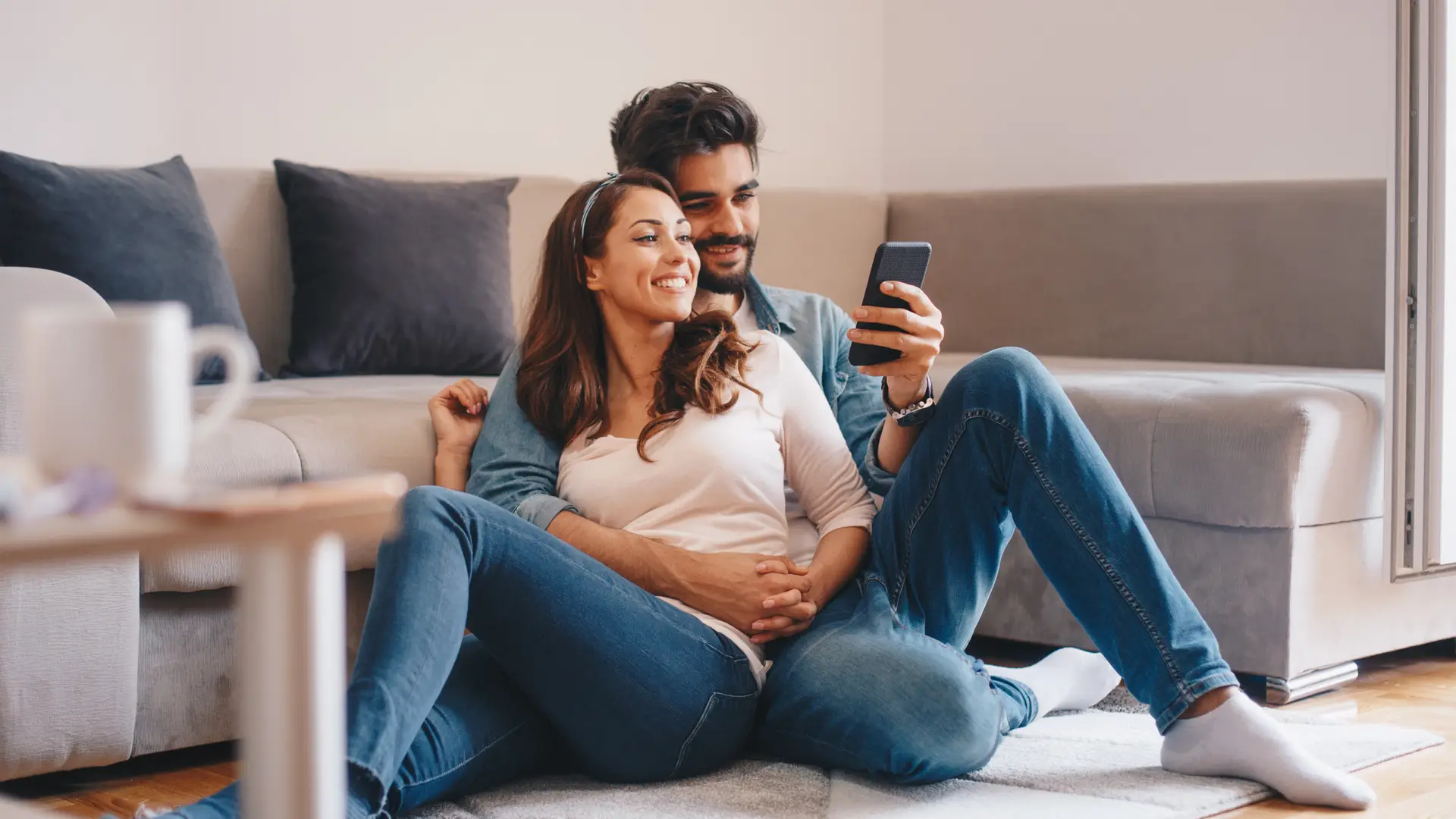 Pareja viendo smartphone tumbados en el suelo de su hogar con seguro de ama contratado Pareja viendo smartphone tumbados en el suelo de su hogar con seguro de ama contratado