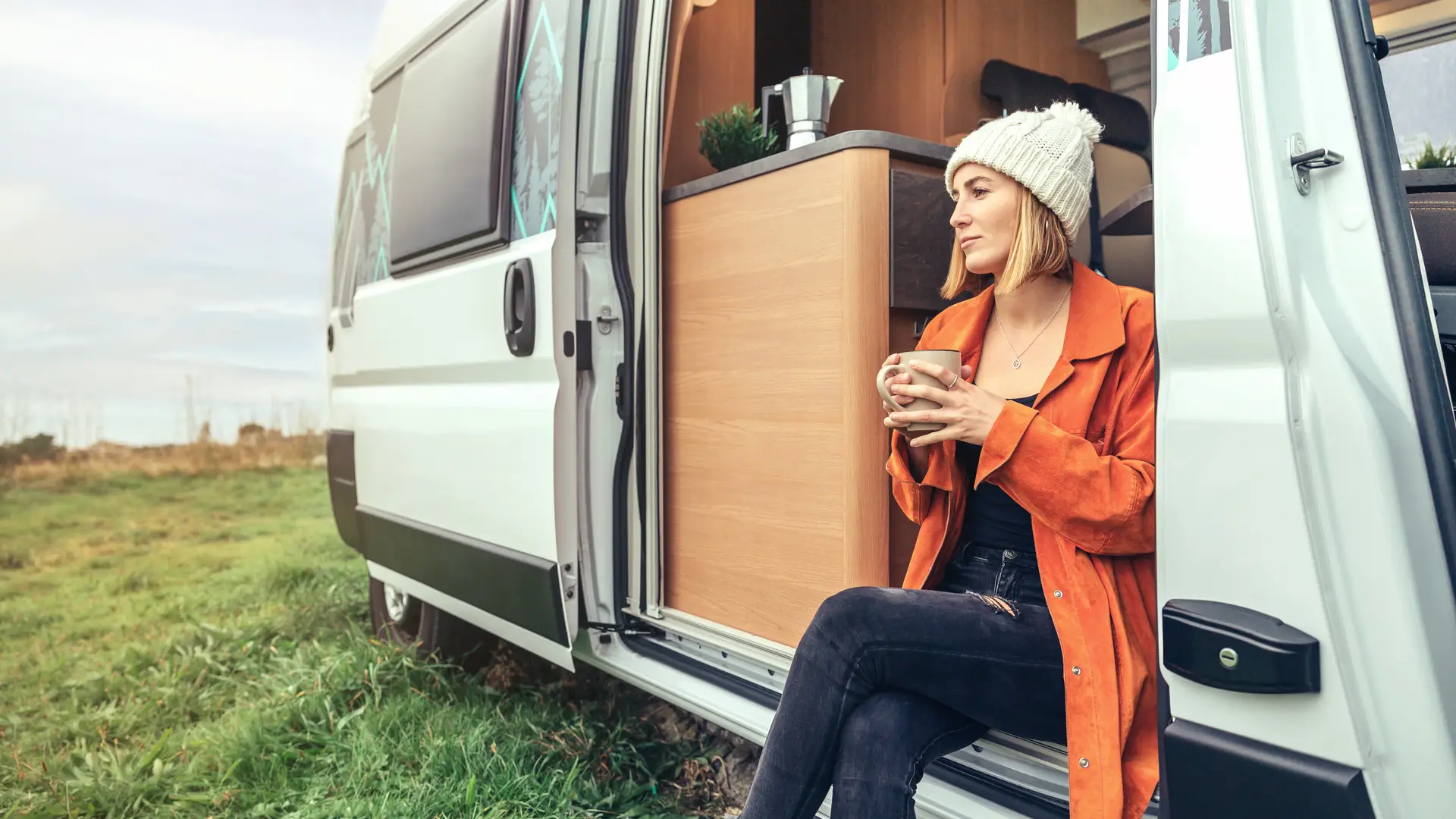 Joven disfrutando de un café en su autocaravana a pie del mar asegurado con axa