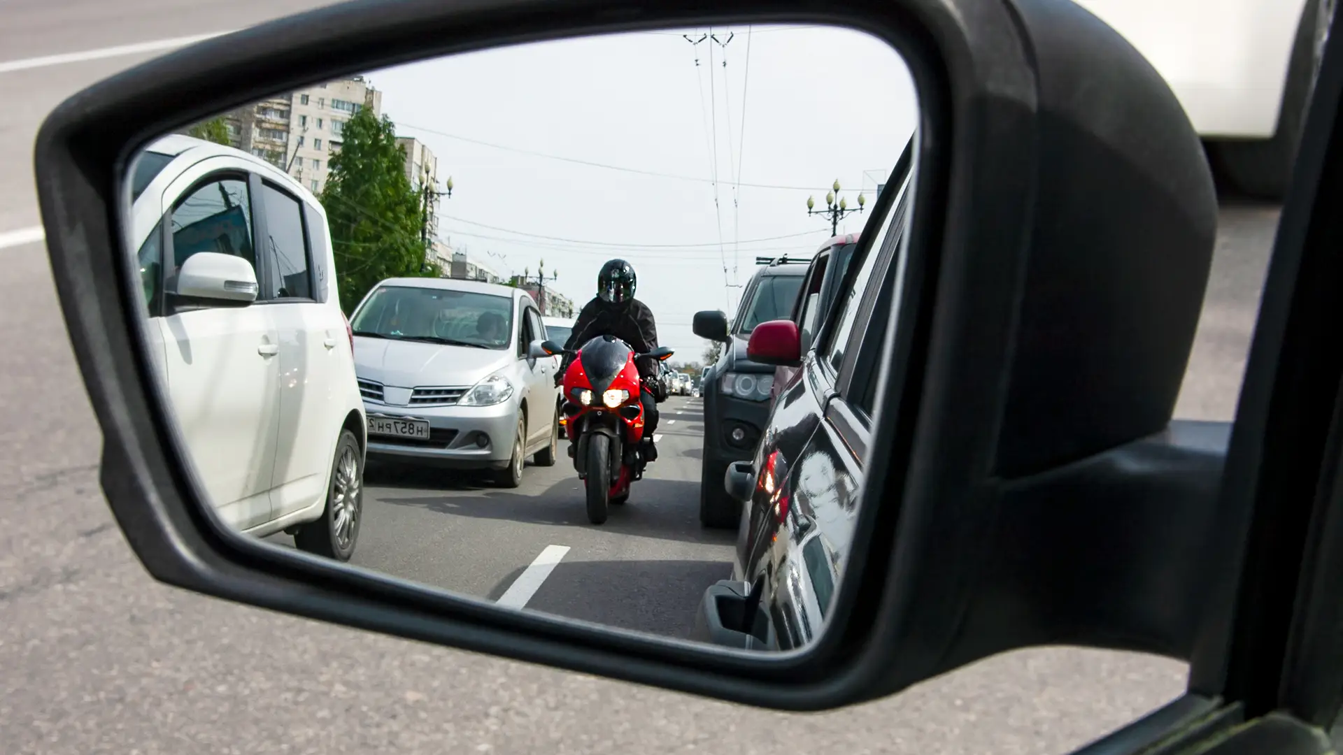 Un motero conduciendo entre los coches visto en un retrovisor que tiene un seguro de moto de Balumba