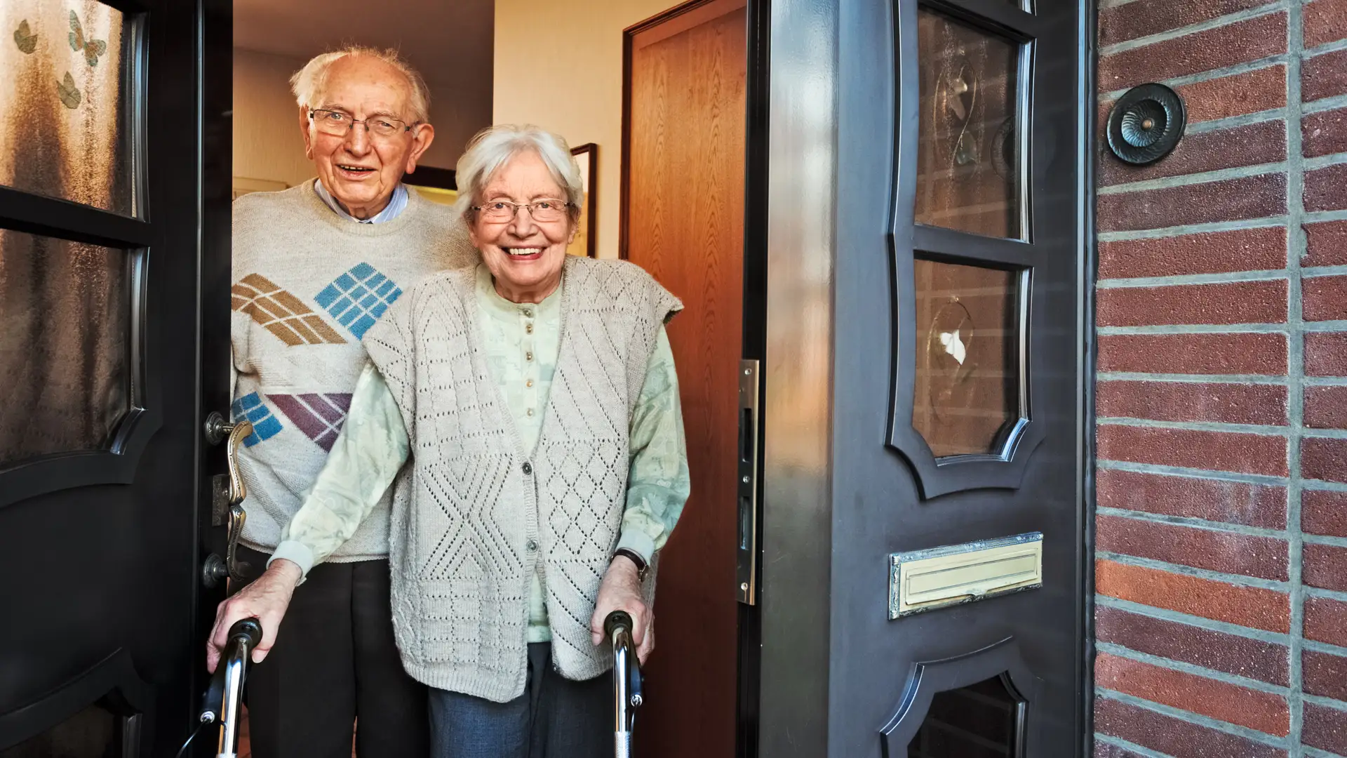 Dos ancianos en la puerta de su casa sonriendo porque tienen un seguro de hogar especial para mayores de Caser