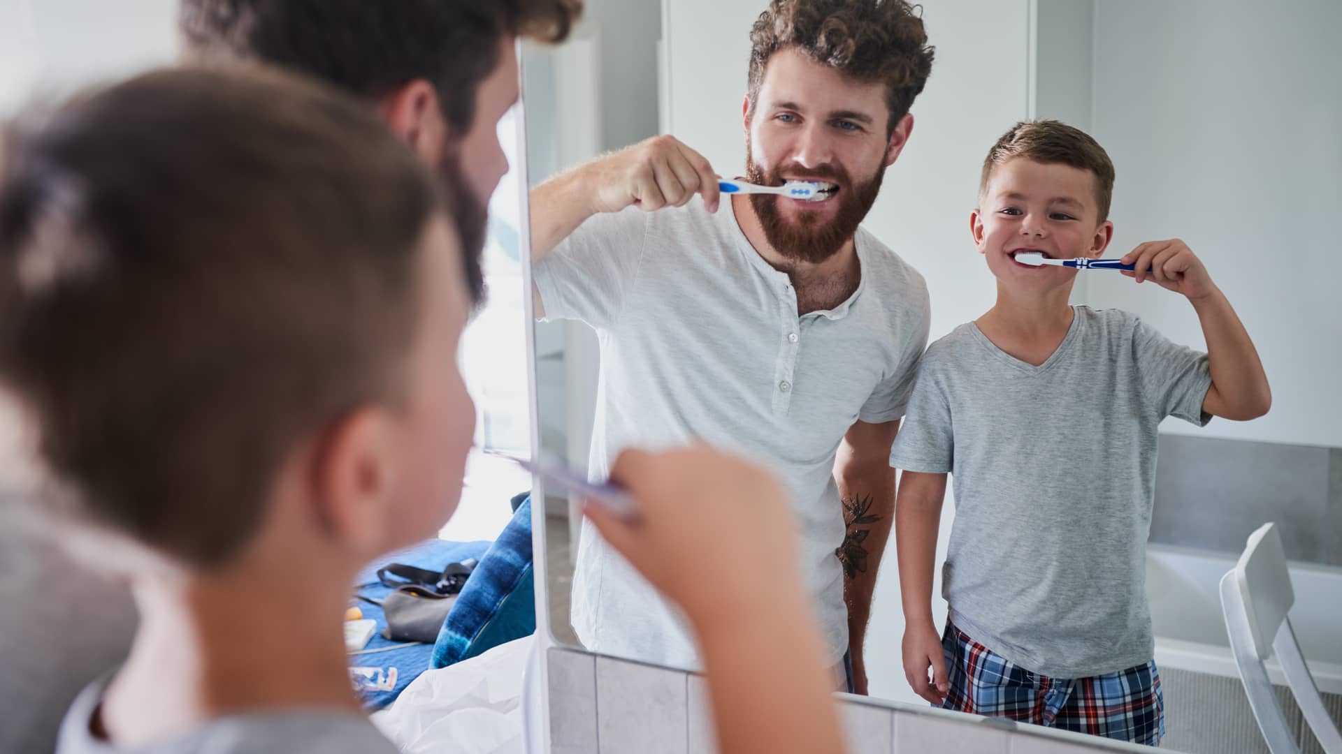 Padre e hijo con seguro dental en cigna cepillandose los dientes frente al espejo