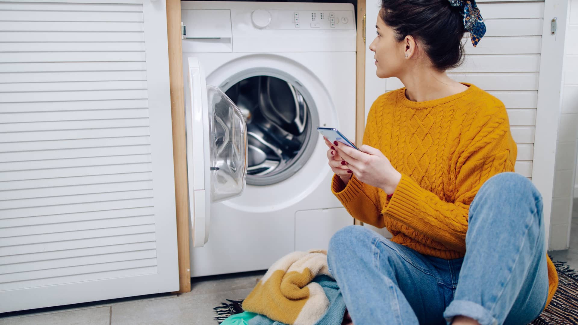 Mujer buscando teléfono de su seguro de línea directa para dar parte al seguro de incidencia con su lavadora Mujer buscando teléfono de su seguro de línea directa para dar parte al seguro de incidencia con su lavadora