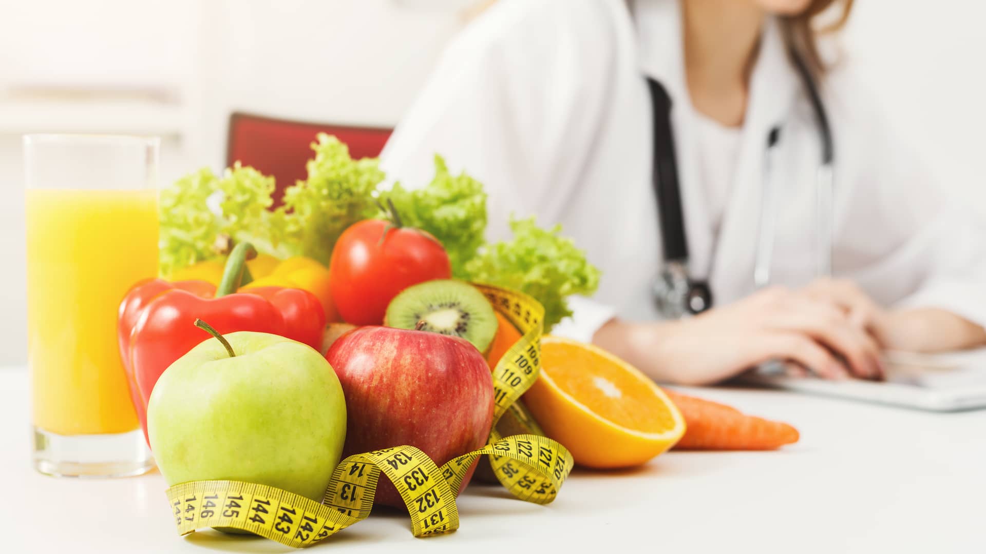 Montaña de frutas con una cinta médica apoyadas sobre una mesa delante de una nutricionista del cuadro médico de Mapfr