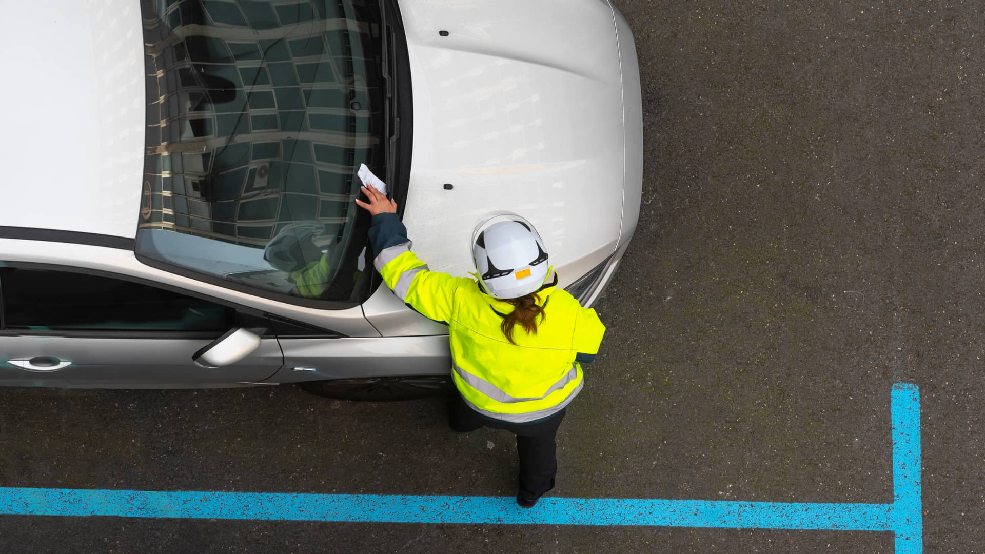 Agente de la policía colocando una multa de tráfico en el parabrisas del coche de un cliente de Mapfre