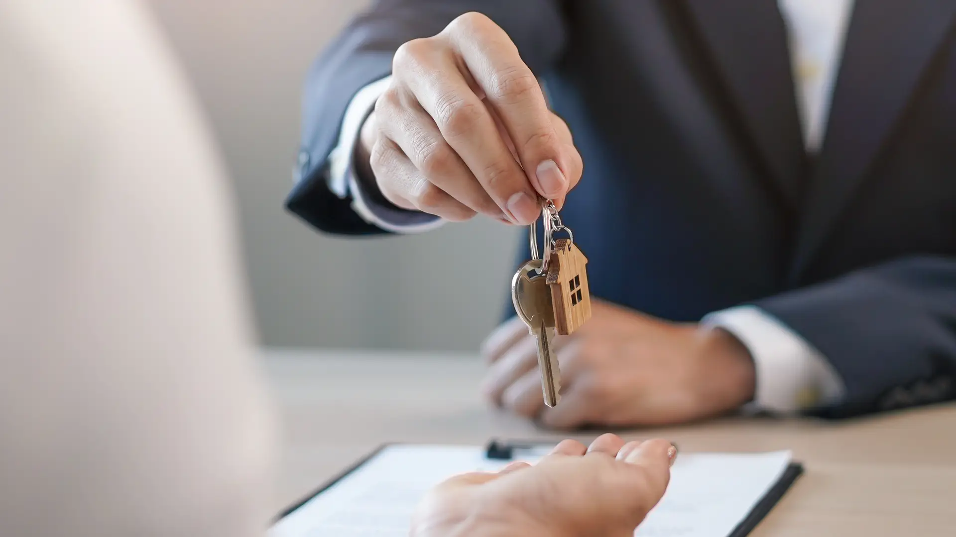 Mano entregando las llaves de una casa con un contrato de seguros de arrendamiento de Mapfre sobre la mesa Mano entregando las llaves de una casa con un contrato de seguros de arrendamiento de Mapfre sobre la mesa