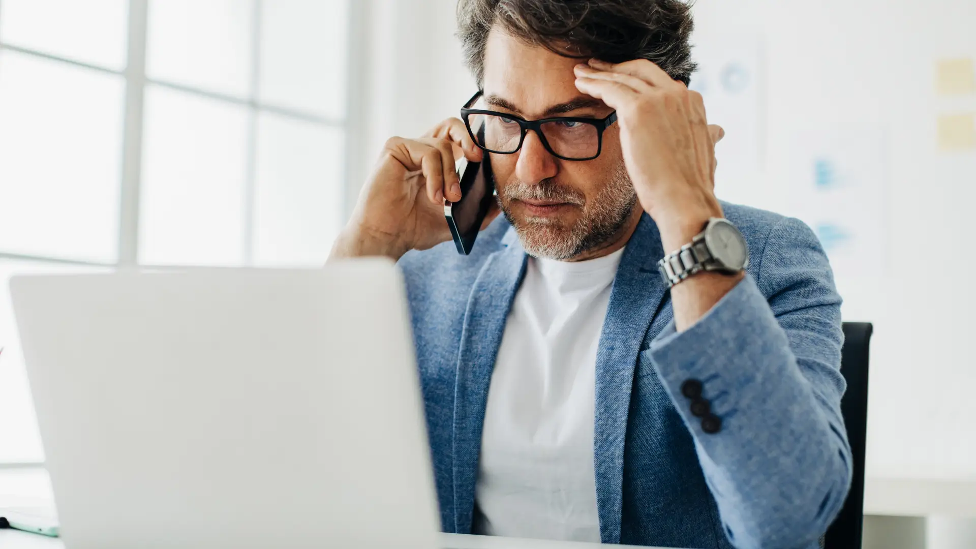 Hombre con gesto serio con el ordenador llamando por teléfono para dar de baja sus seguros de Metlife