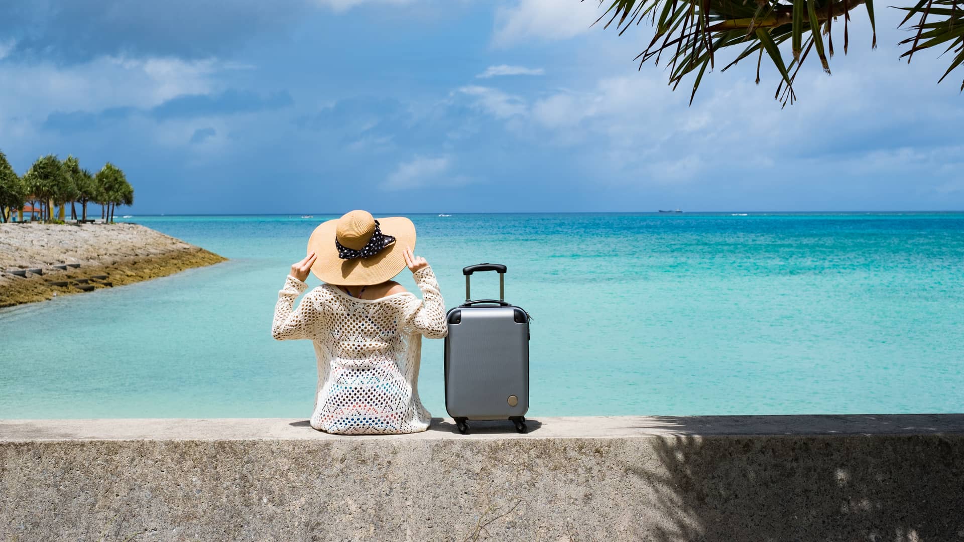 Mujer sentada con su maleta frente a su destino vacacional con seguro de viaje ocaso contratado Mujer sentada con su maleta frente a su destino vacacional con seguro de viaje ocaso contratado