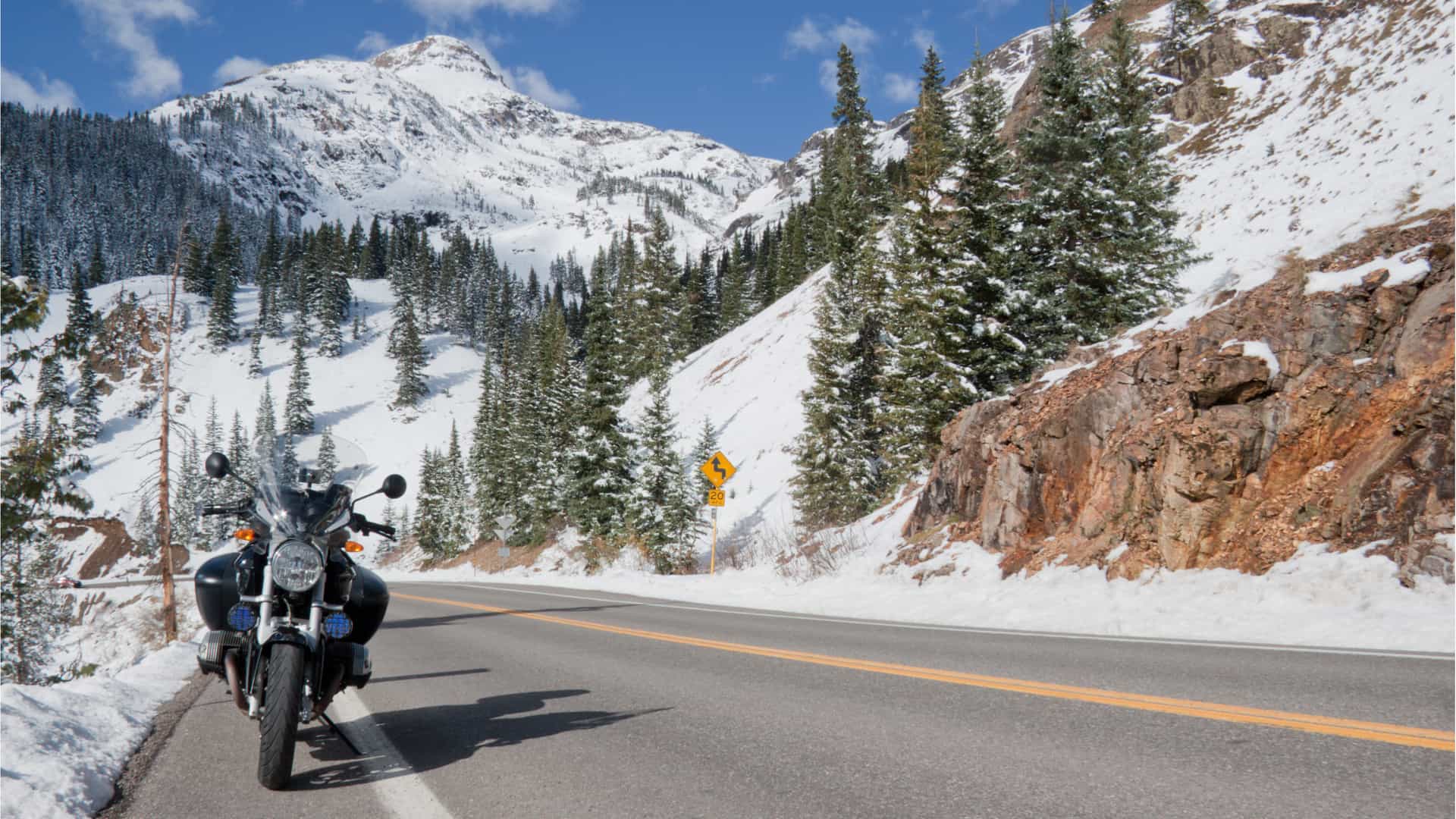 Hombre fotografiando su moto asegurada con seguro pleayo y estacionada en el arcen de una carretera con paisaje nevado Hombre fotografiando su moto asegurada con seguro pleayo y estacionada en el arcen de una carretera con paisaje nevado