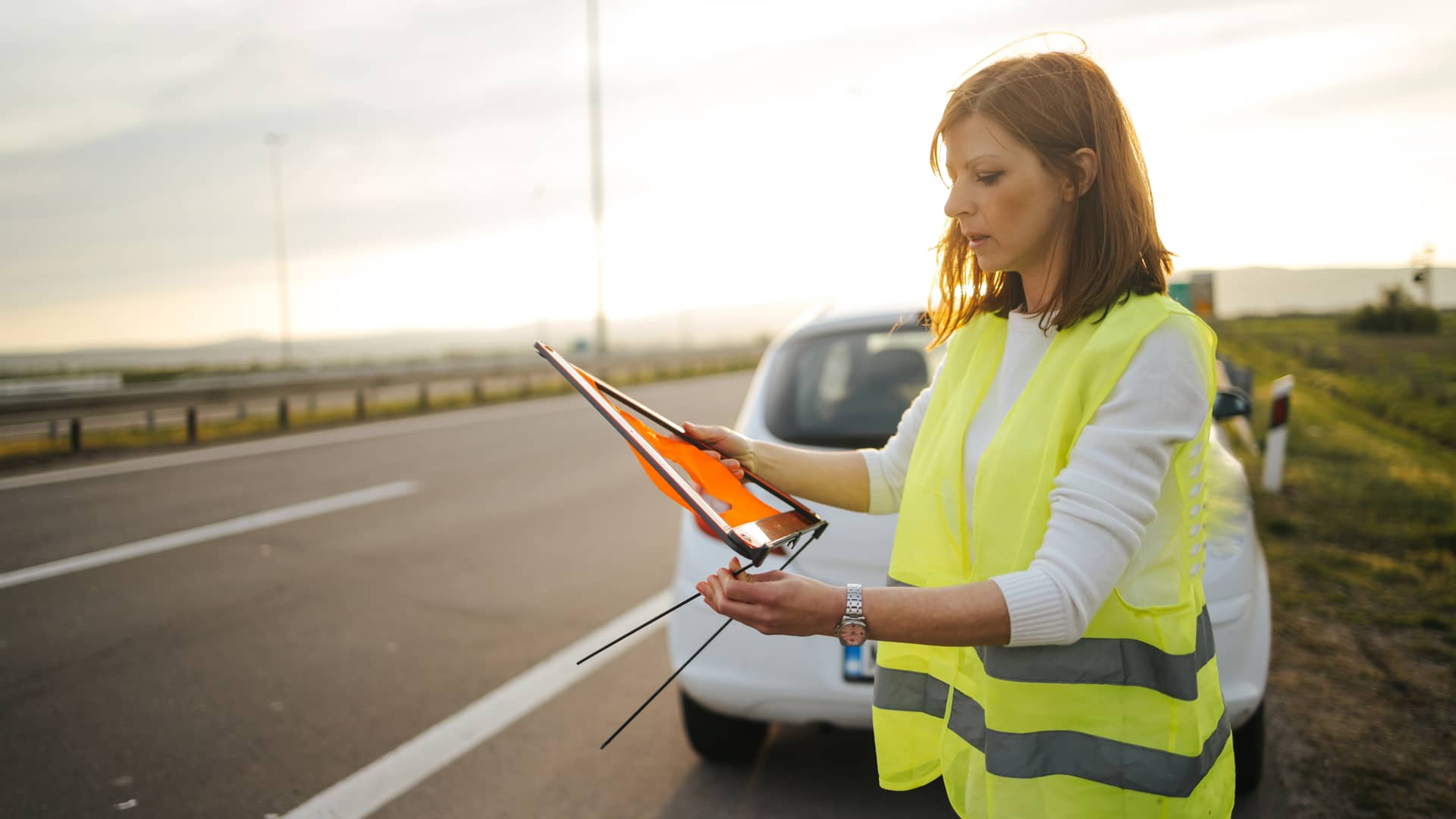 Mujer colocando los triangulos en la carretera esperando asistencia de grua de su seguro de coche de plus ultra Mujer colocando los triangulos en la carretera esperando asistencia de grua de su seguro de coche de plus ultra