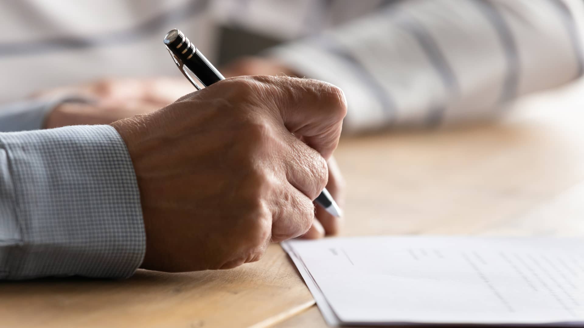 Manos de un anciano firmando los papeles para dar de baja su seguros con Qualitas Auto