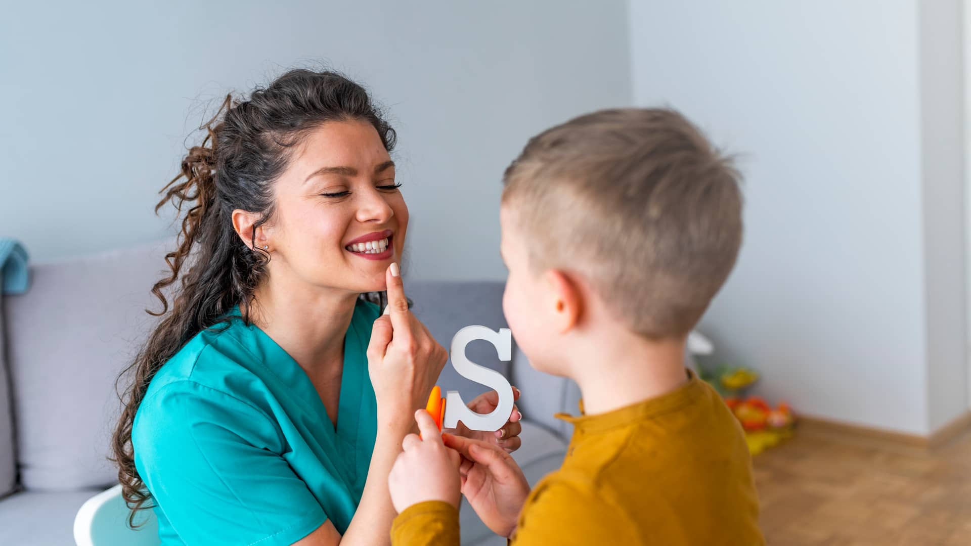 Una logopeda de Sanitas enseñando a un niño pequeño como colocar la lengua para pronunciar las letras