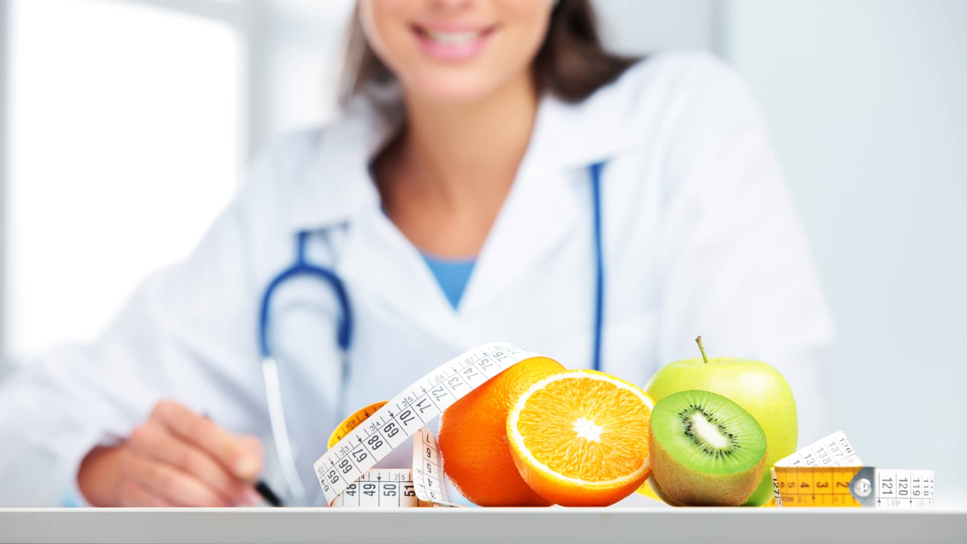 Montaña de frutas con una cinta médica frente a una nutricionista del cuadro médico de Sanitas