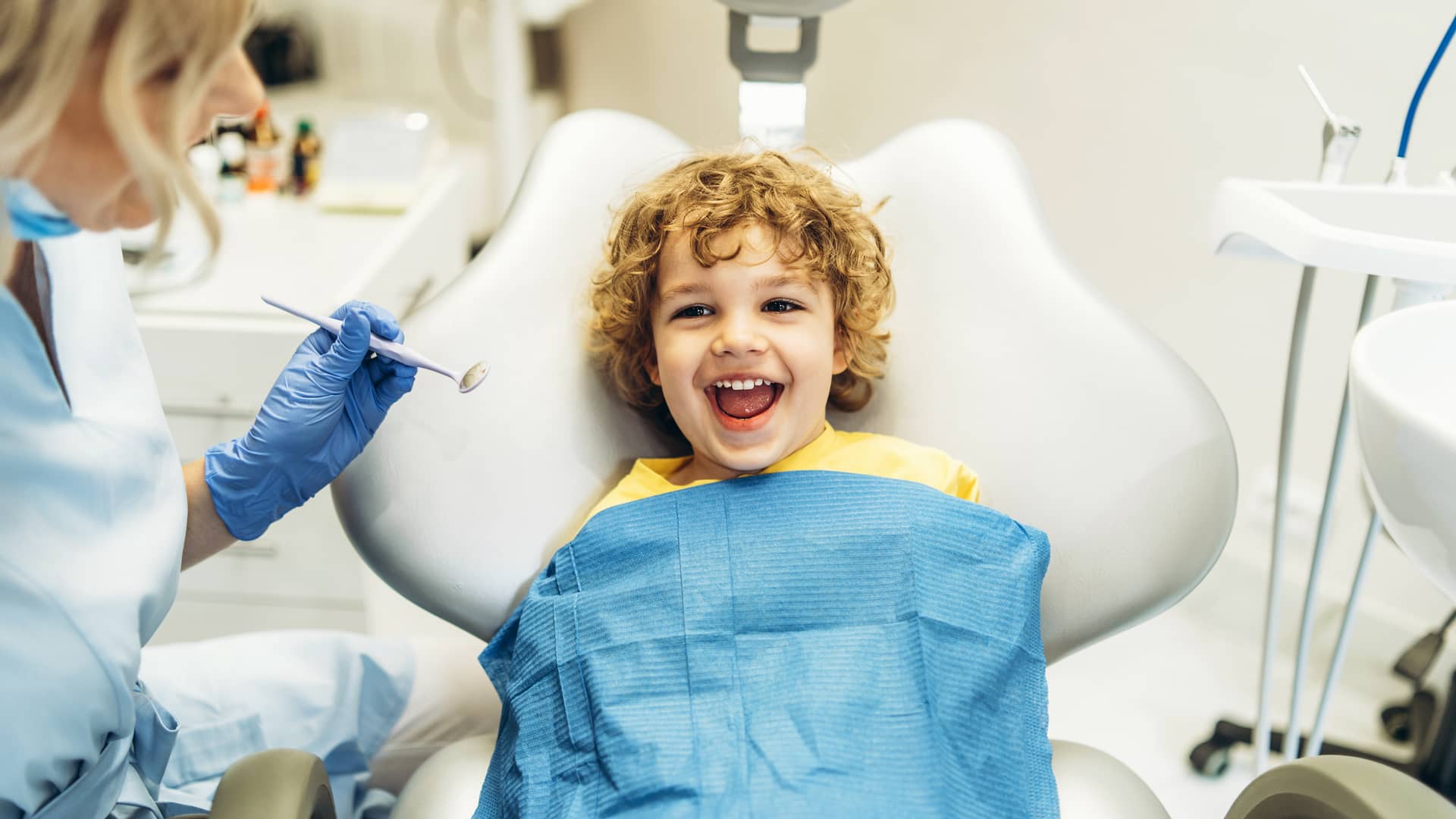 Niño pequeño de rizos sonriendo en la consulta del dentista porque tiene seguro dental premium de Sanitas Niño pequeño de rizos sonriendo en la consulta del dentista porque tiene seguro dental premium de Sanitas