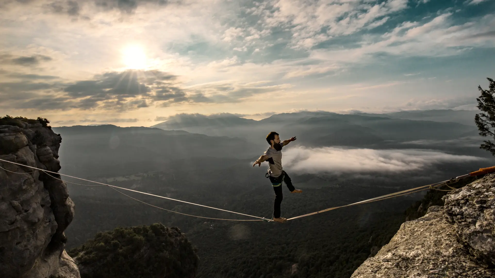Hombre con seguro de vida contratado con santalucia cruzando de una montaña a otra por un cable de acero Hombre con seguro de vida contratado con santalucia cruzando de una montaña a otra por un cable de acero