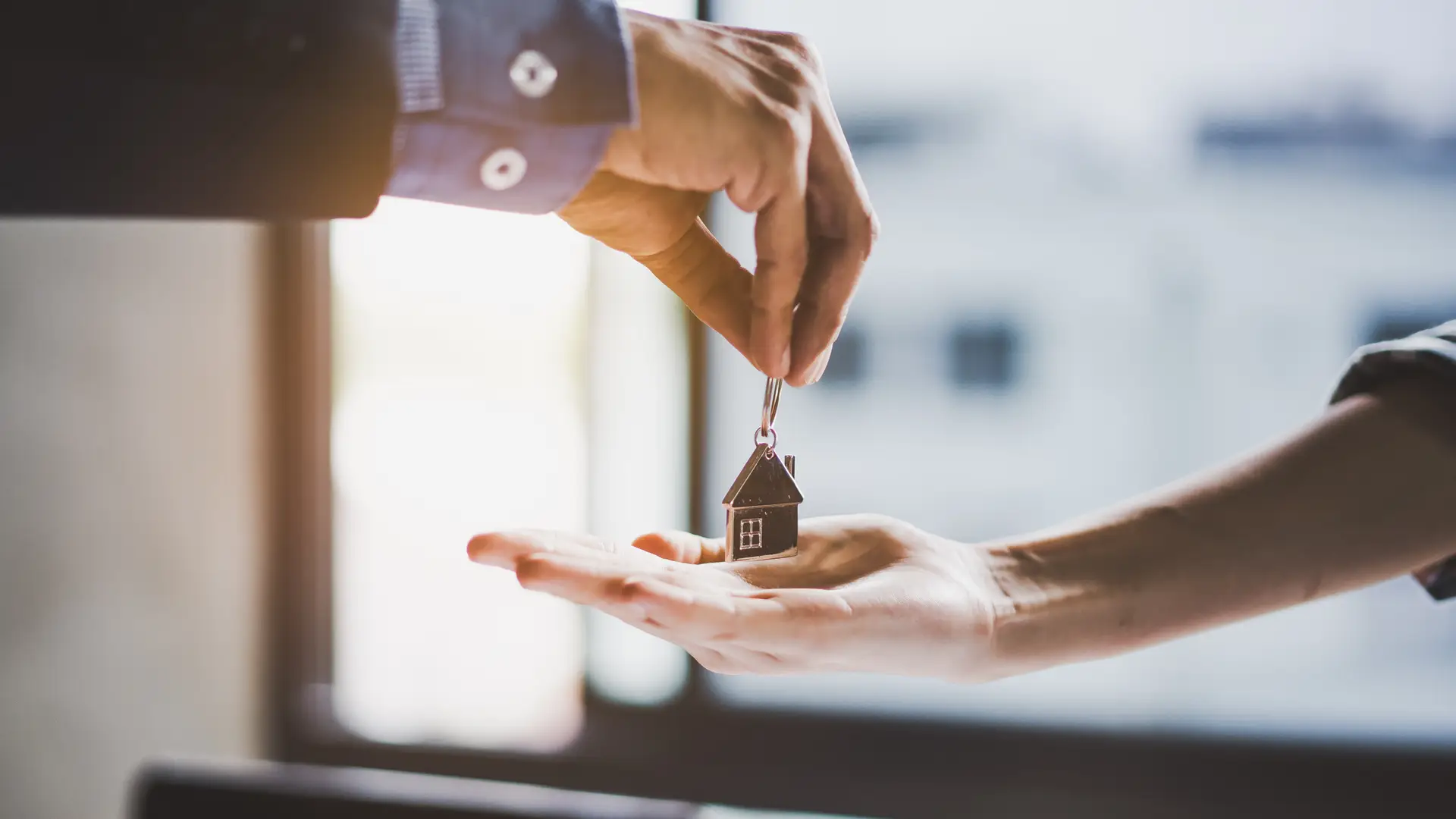 una mano dandole a otra un llavero de una casa que representa el seguro de arrendamiento una mano dandole a otra un llavero de una casa que representa el seguro de arrendamiento