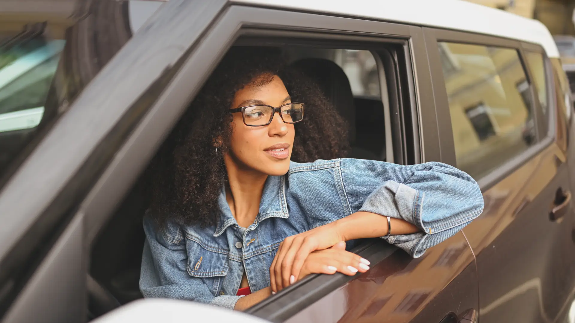 Joven mirando por la ventanilla sentada en su coche sín carnet Joven mirando por la ventanilla sentada en su coche sín carnet