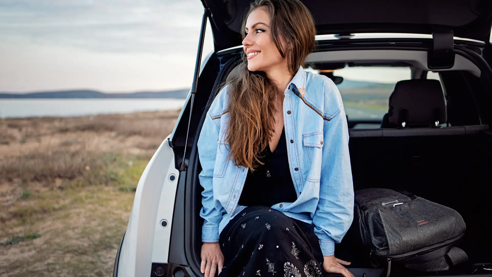 Mujer sentada en el maletero de su coche pensando en si renovar el seguro de su coche con la misma compañía