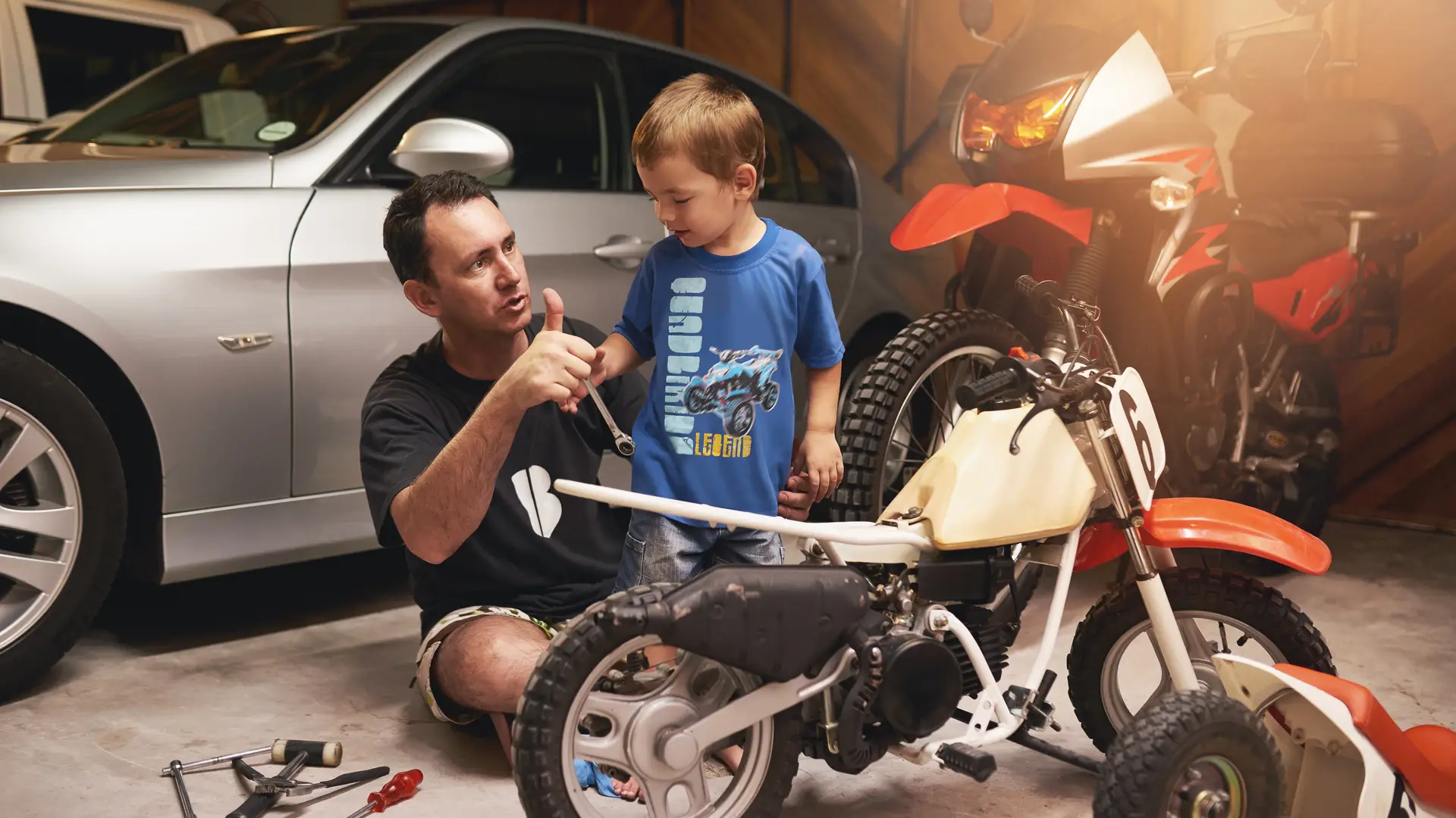 Padre enseñando a su hijo a arreglar su moto en el garaje de su casa en el cual tiene sus vehículos con un seguro combinado Padre enseñando a su hijo a arreglar su moto en el garaje de su casa en el cual tiene sus vehículos con un seguro combinado