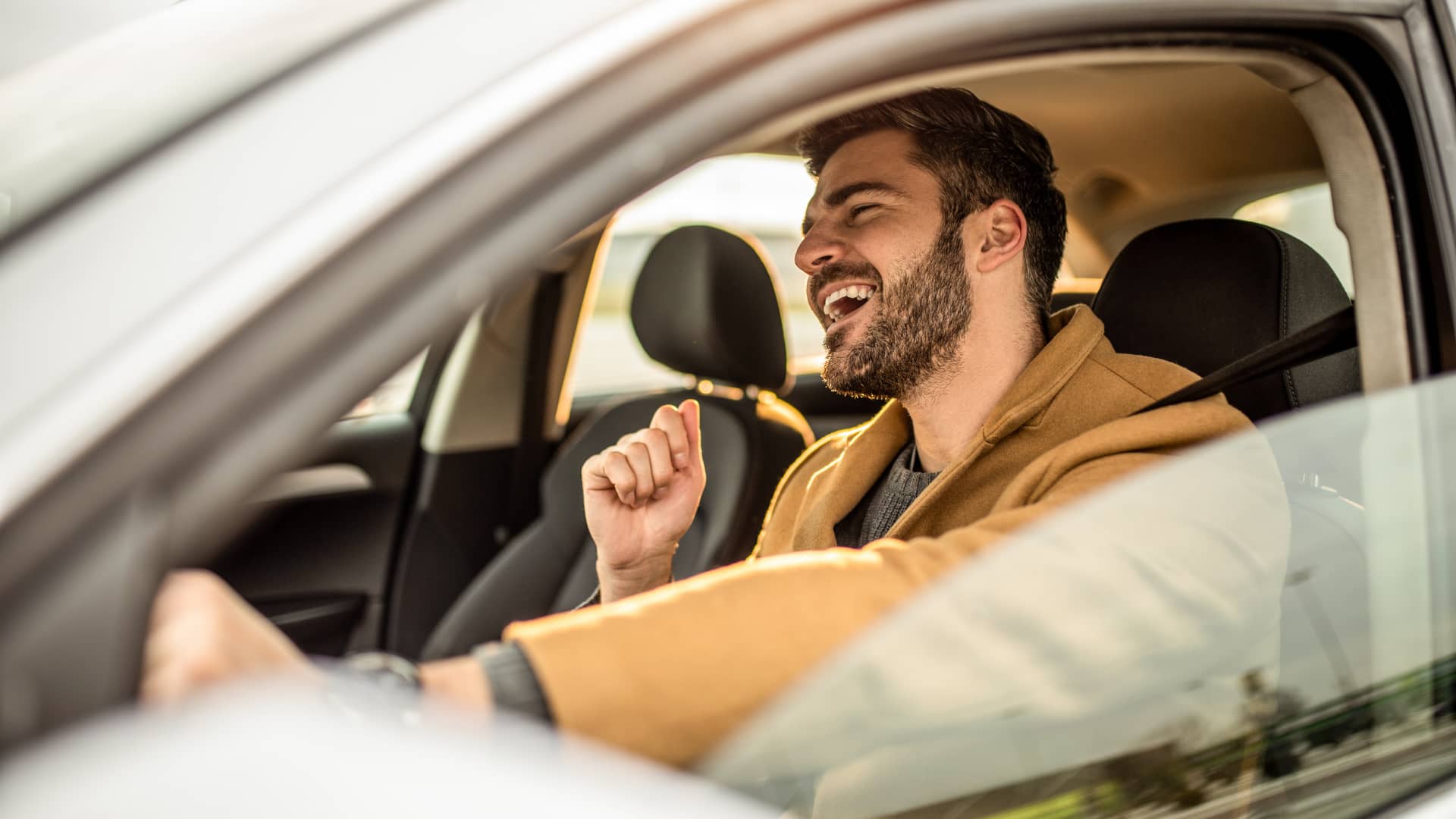 Hombre sonriente cantando en su coche con seguro a terceros contratado