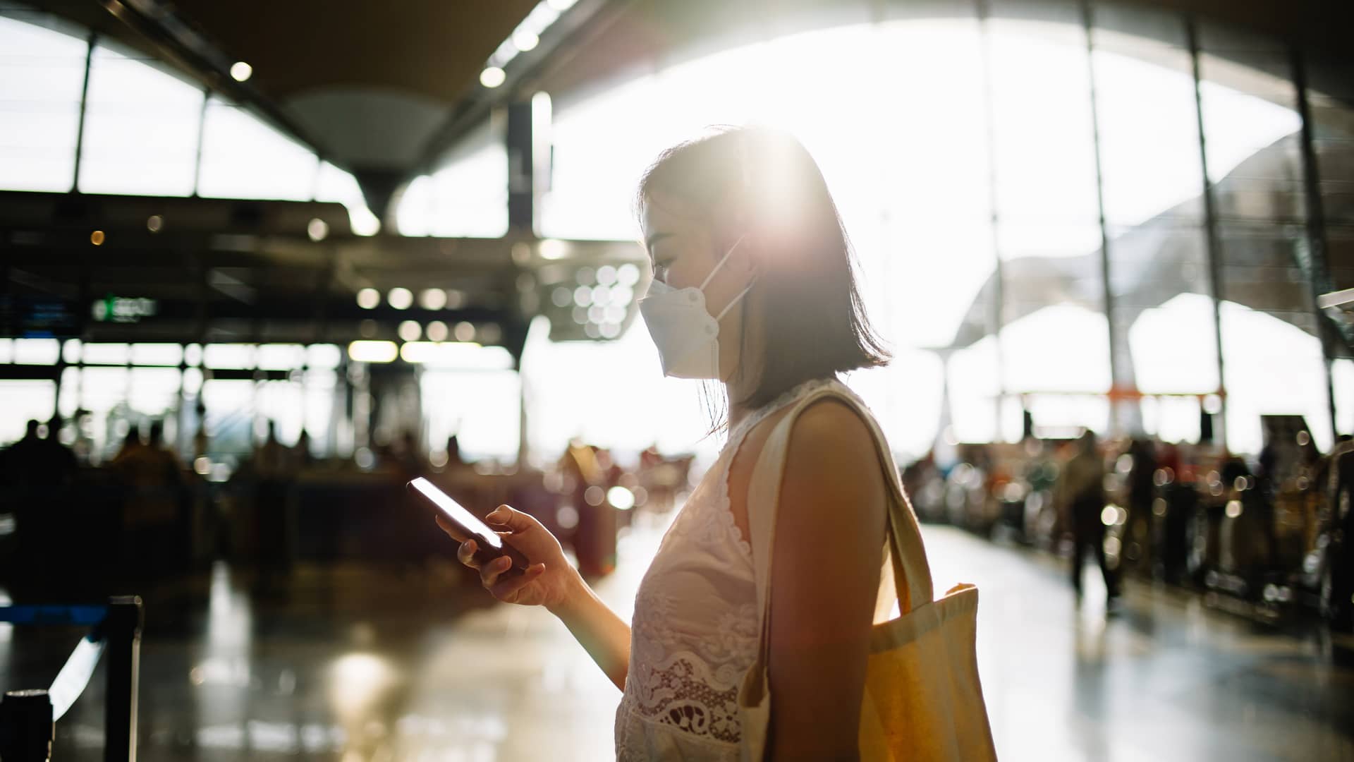 Mujer asiática con mascarilla y buscando en su móvil su certificado de seguro de viaje para mostrar a personal Mujer asiática con mascarilla y buscando en su móvil su certificado de seguro de viaje para mostrar a personal