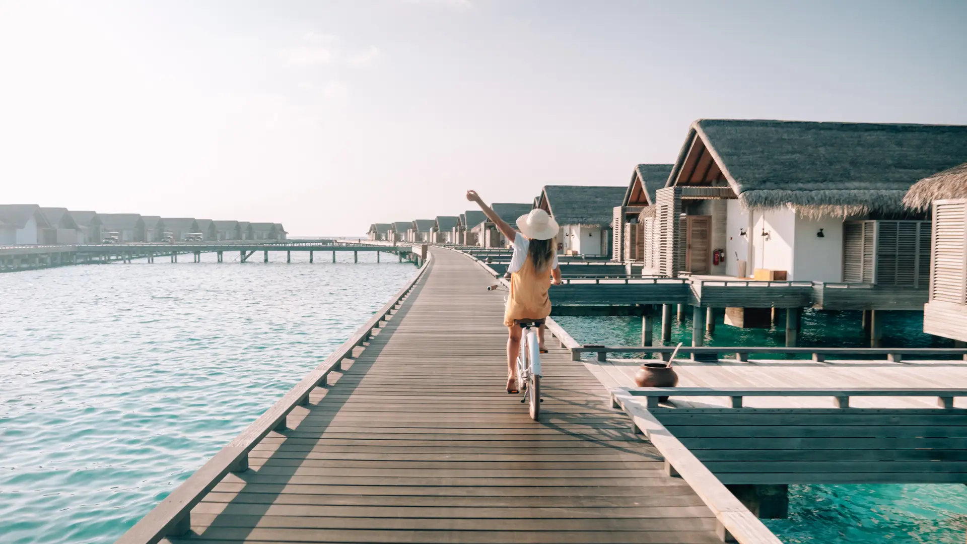 Joven montando en bicicleta en el muelle de madera en las Maldivas para cuyo viaje ha contratado un seguro Joven montando en bicicleta en el muelle de madera en las Maldivas para cuyo viaje ha contratado un seguro