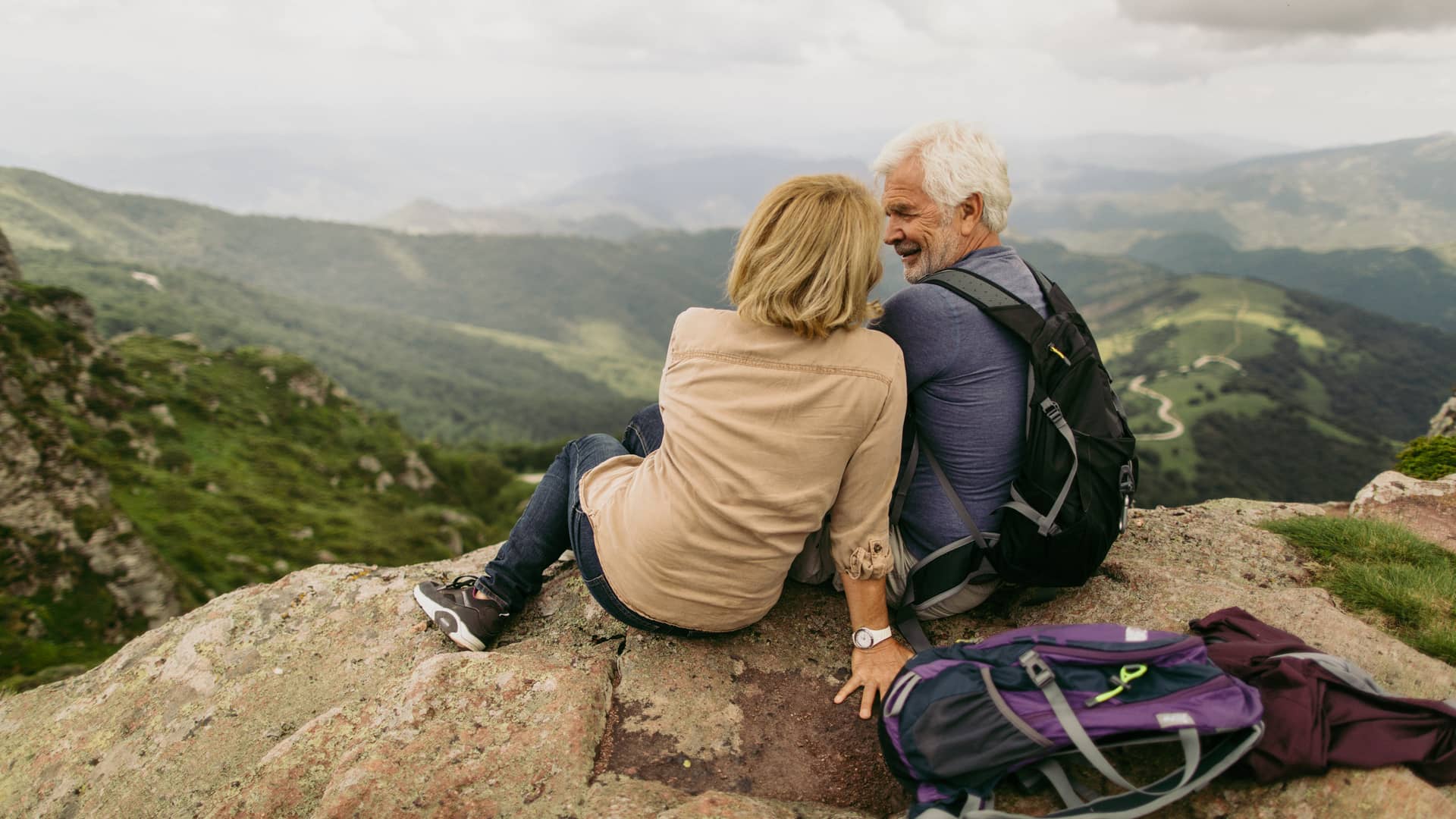 Pareja de la tercera edad disfrutando de las vistas desde arriba de la montaña y con la seguridad que les da tener un seguro de viaje para mayores Pareja de la tercera edad disfrutando de las vistas desde arriba de la montaña y con la seguridad que les da tener un seguro de viaje para mayores