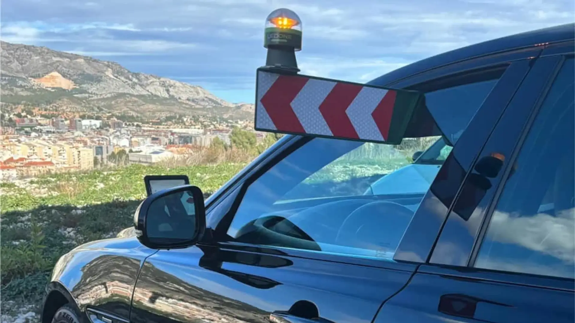 Coche equipado con una baliza de emergencia V-16 conectada y paneles reflectantes en una carretera de montaña.