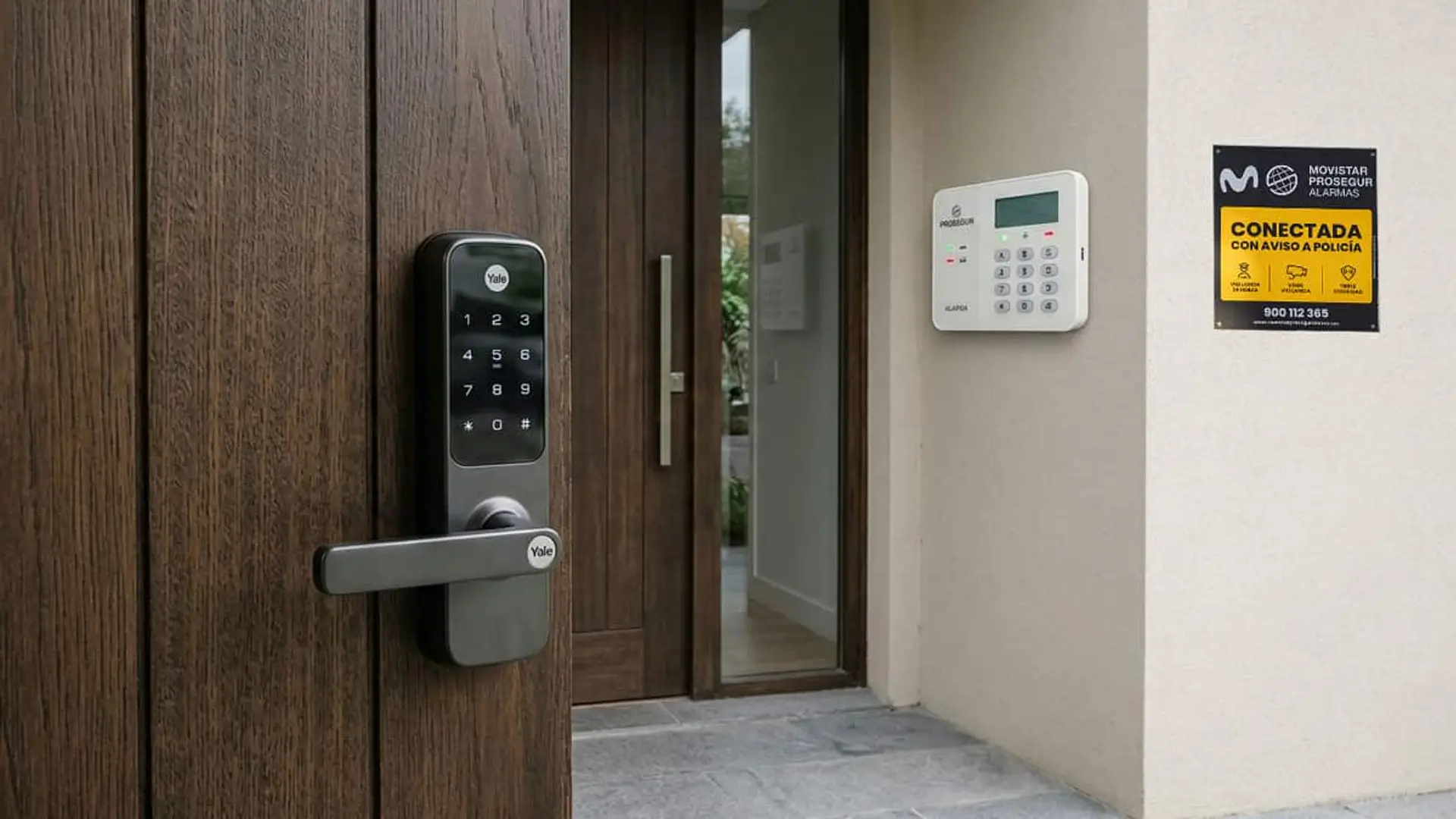 Puerta de madera con cerradura electrónica Yale y teclado de alarma Movistar Prosegur, junto a una placa de alarma conectada con aviso a la policía.
