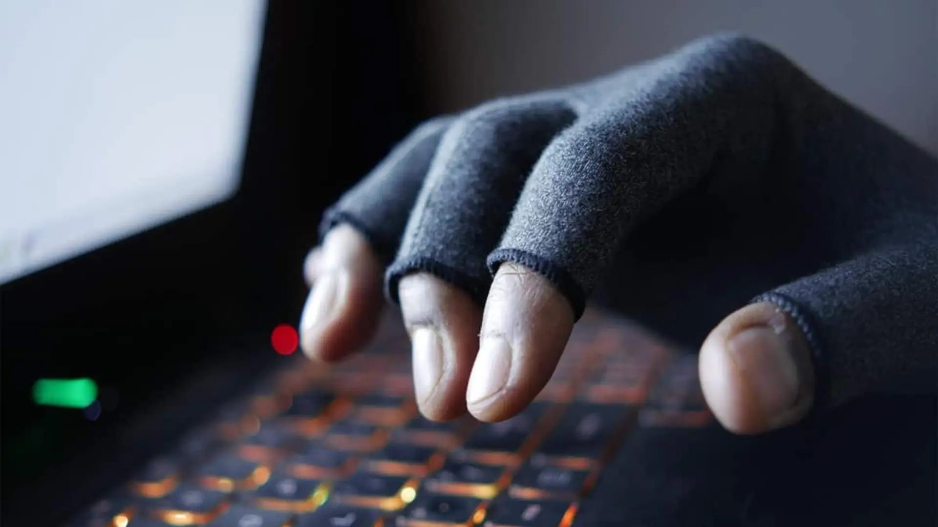 La red WiFi para invitados no aísla tus dispositivos como creías: esto es lo que falla Mano con guante escribiendo en un teclado iluminado, representando un posible ciberataque o actividad de hacking.